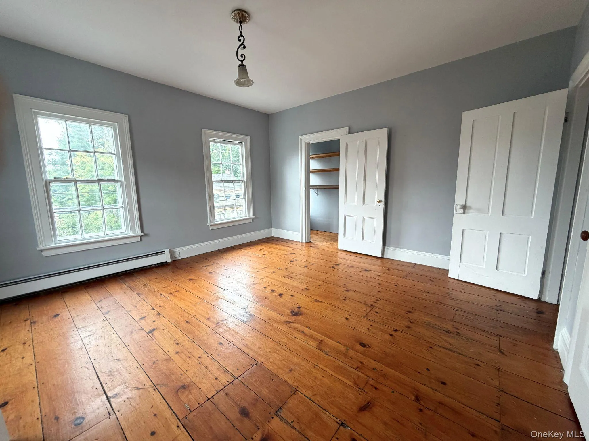 Hardwood flooring, two sash windows, a built-in closet with shelving, a four-panel door, and a ceiling-mounted light fixture Hardwood flooring, two sash windows, a built-in closet with shelving, a four-panel door, and a ceiling-mounted light fixture