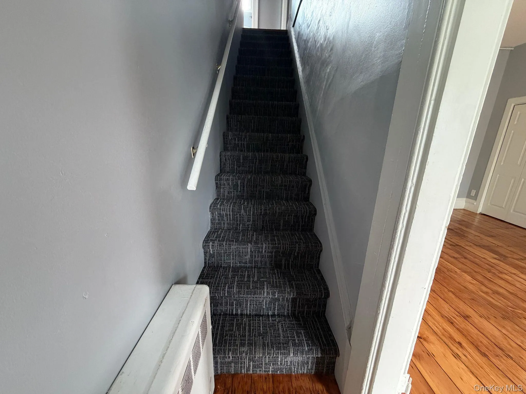Staircase featuring patterned carpet runner, white handrail, and light-toned wall paint Staircase featuring patterned carpet runner, white handrail, and light-toned wall paint
