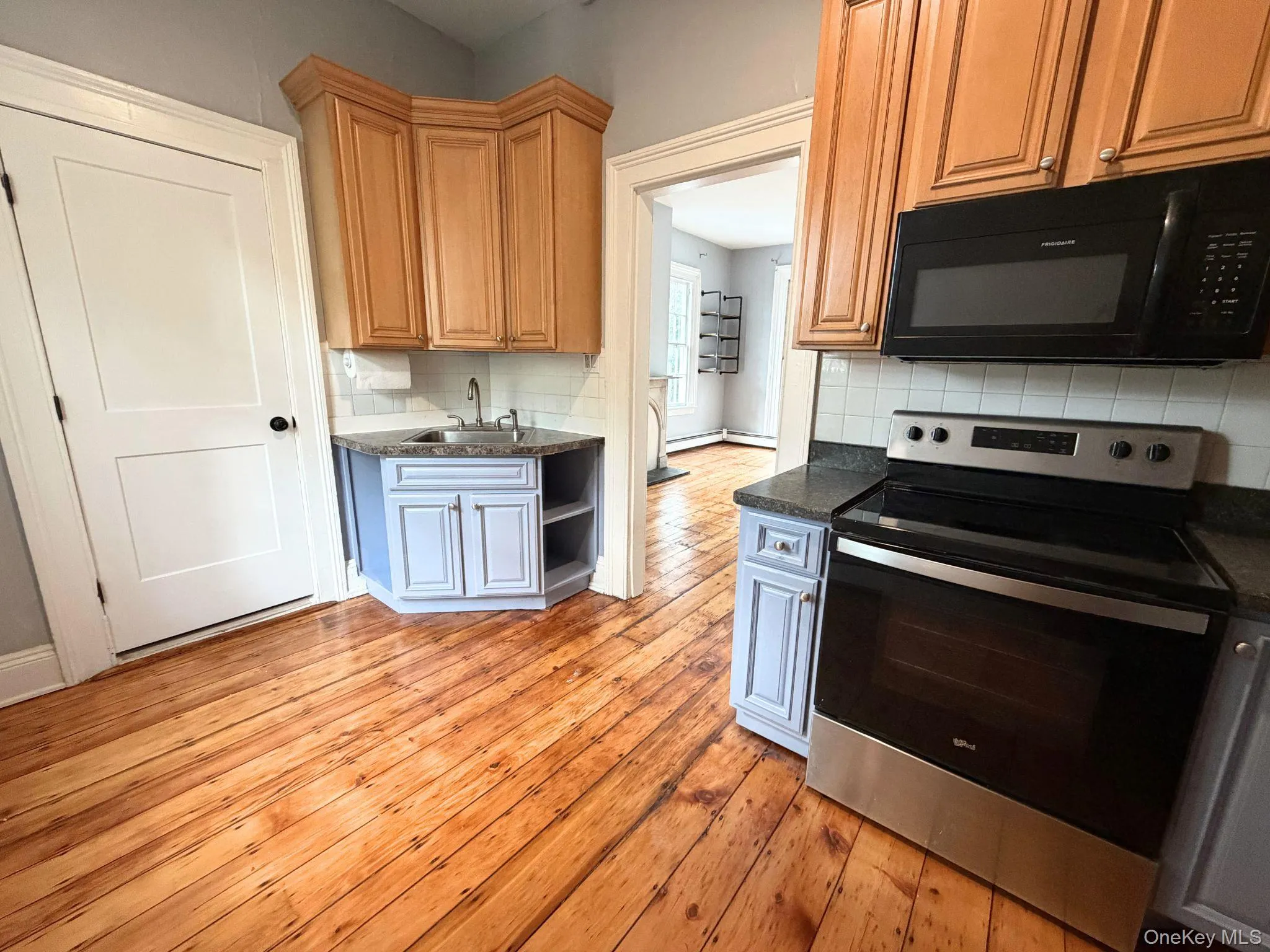 Kitchen featuring wood-finish flooring, two-tone cabinetry, dark countertops, a stainless steel range, and an over-the-range microwave Kitchen featuring wood-finish flooring, two-tone cabinetry, dark countertops, a stainless steel range, and an over-the-range microwave