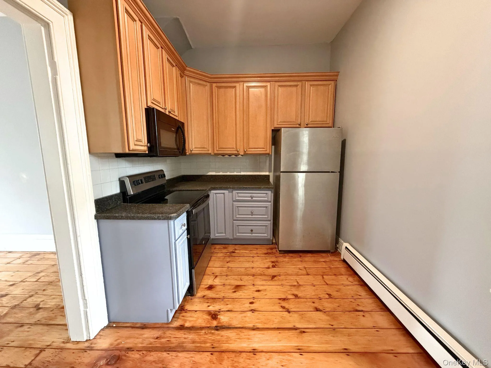 Wood-finish flooring, light wood cabinetry, stainless steel refrigerator, black microwave, and black electric range Wood-finish flooring, light wood cabinetry, stainless steel refrigerator, black microwave, and black electric range