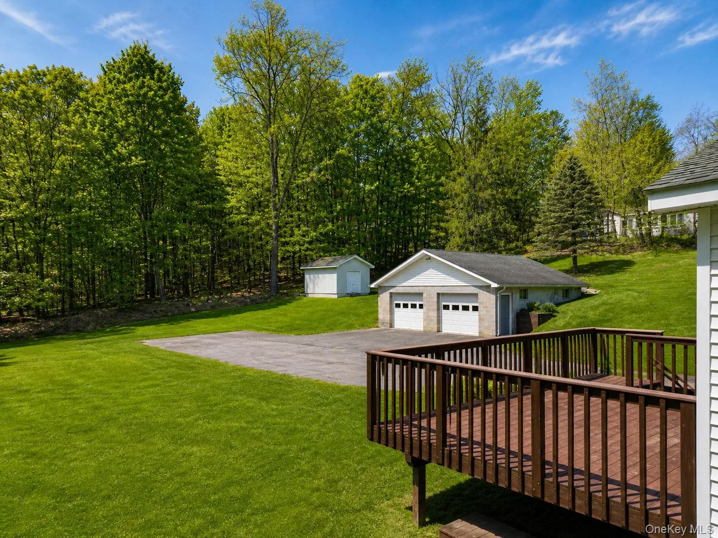 Expansive yard featuring a large wooden deck, a paved driveway, and a two-car garage with white paneled doors Expansive yard featuring a large wooden deck, a paved driveway, and a two-car garage with white paneled doors