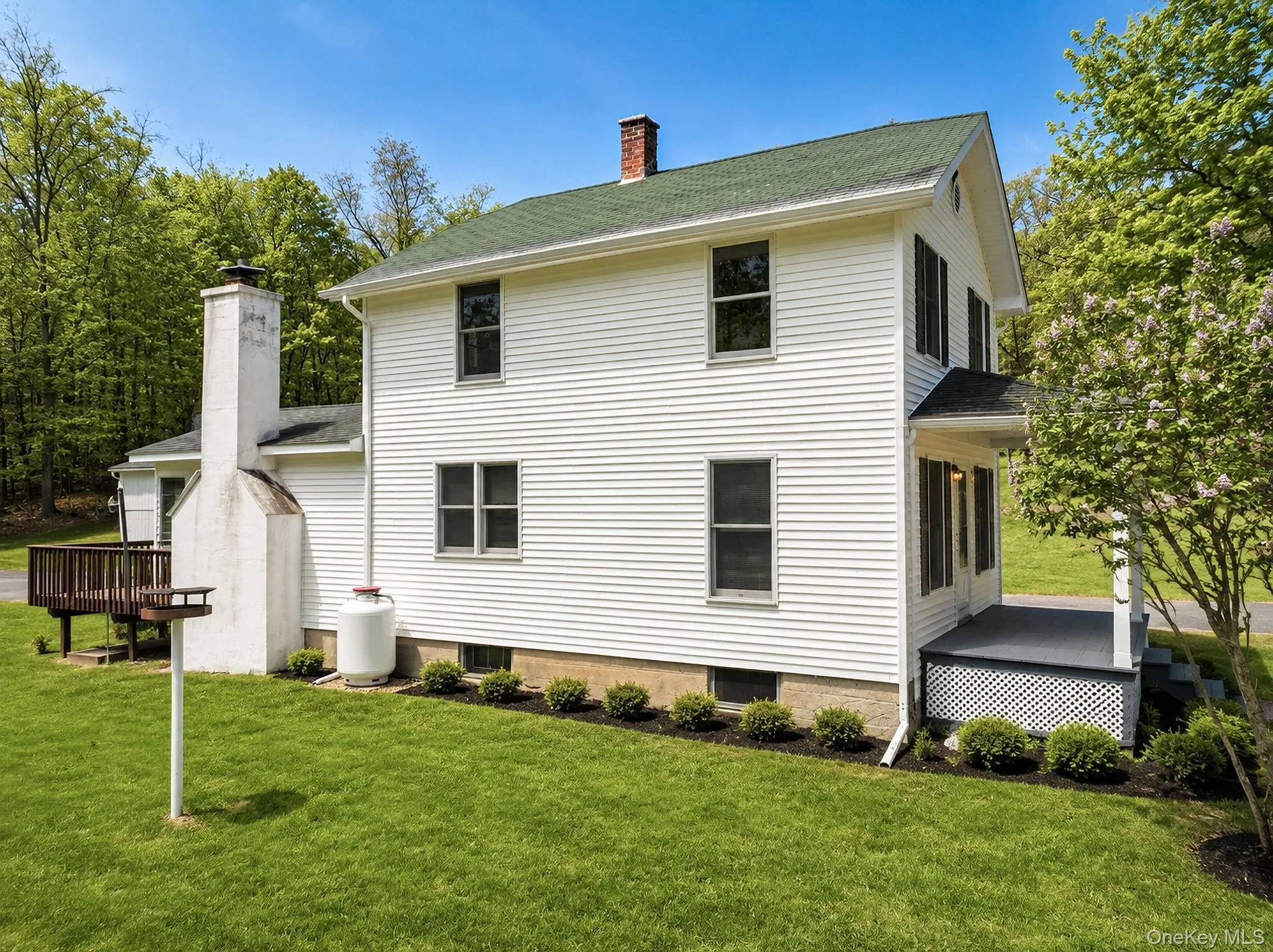 White siding exterior with green roofing, featuring a multi-level deck and a covered porch with lattice detailing White siding exterior with green roofing, featuring a multi-level deck and a covered porch with lattice detailing
