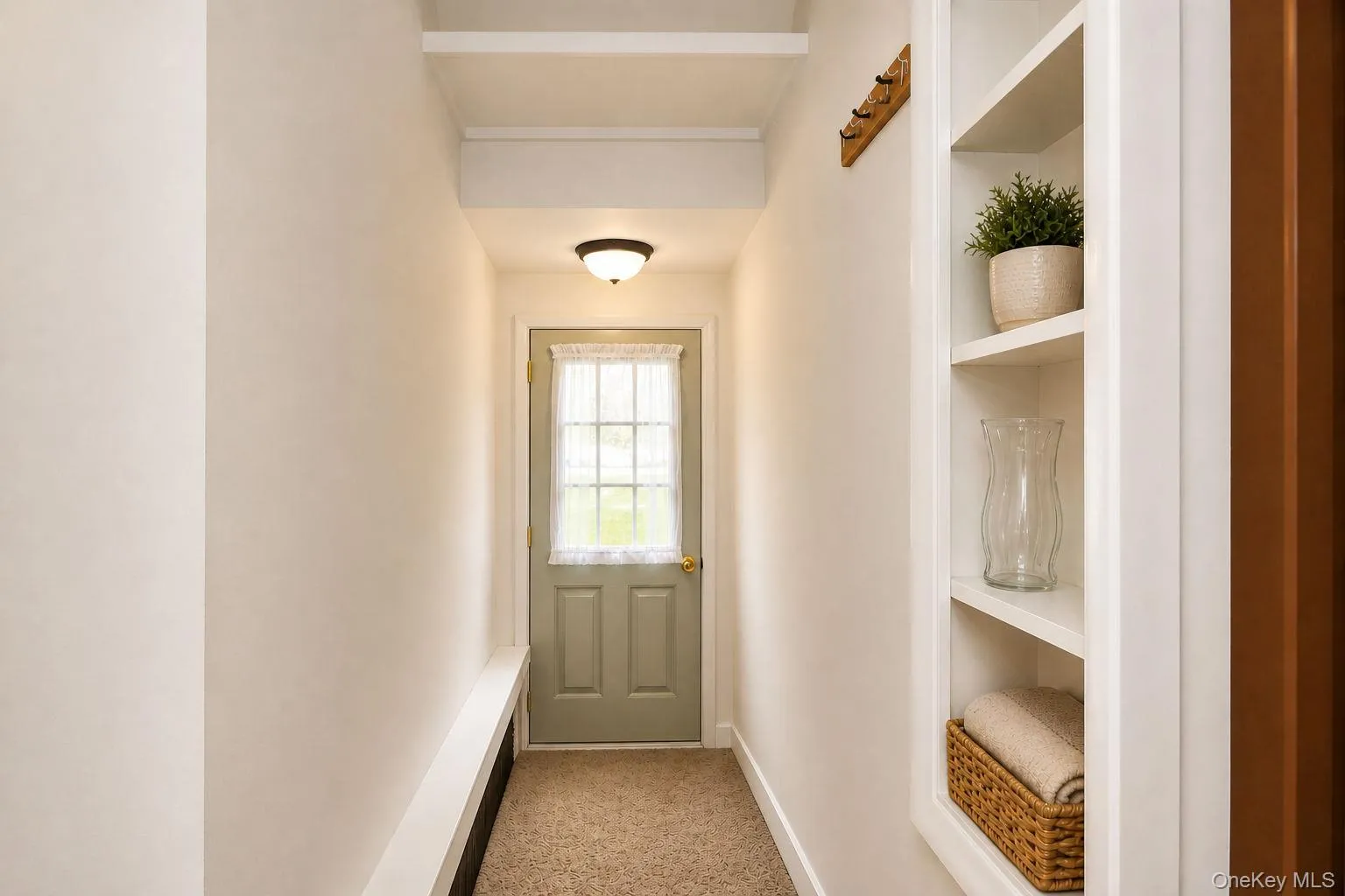 Entryway featuring a light green door with a window, warm-toned carpet, built-in shelving, a recessed wall bench, and overhead lighting Entryway featuring a light green door with a window, warm-toned carpet, built-in shelving, a recessed wall bench, and overhead lighting