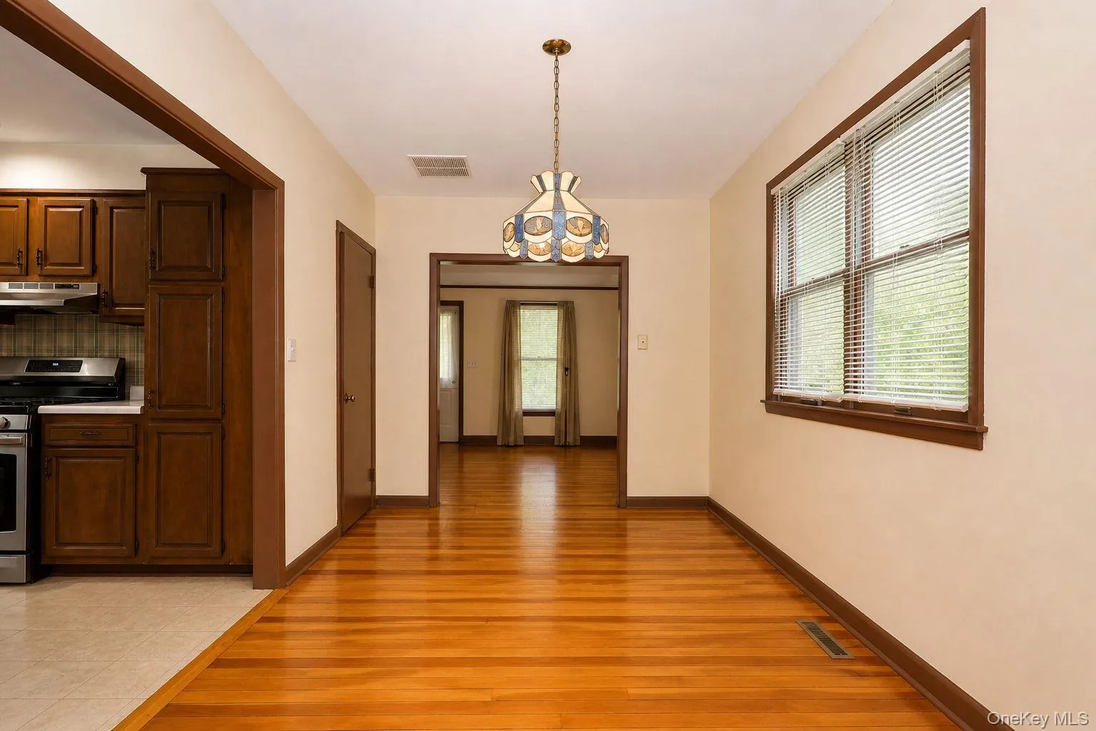 Spacious room featuring wood-finish flooring, a decorative ceiling fixture, and a large window with blinds Spacious room featuring wood-finish flooring, a decorative ceiling fixture, and a large window with blinds