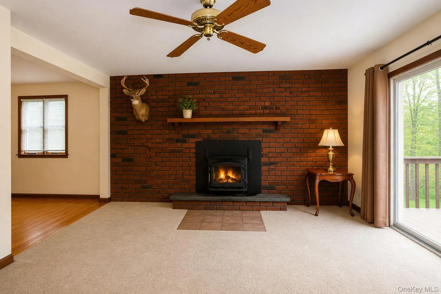 Living area featuring a brick accent wall with a fireplace insert, a wood mantel, and a ceiling fan Living area featuring a brick accent wall with a fireplace insert, a wood mantel, and a ceiling fan