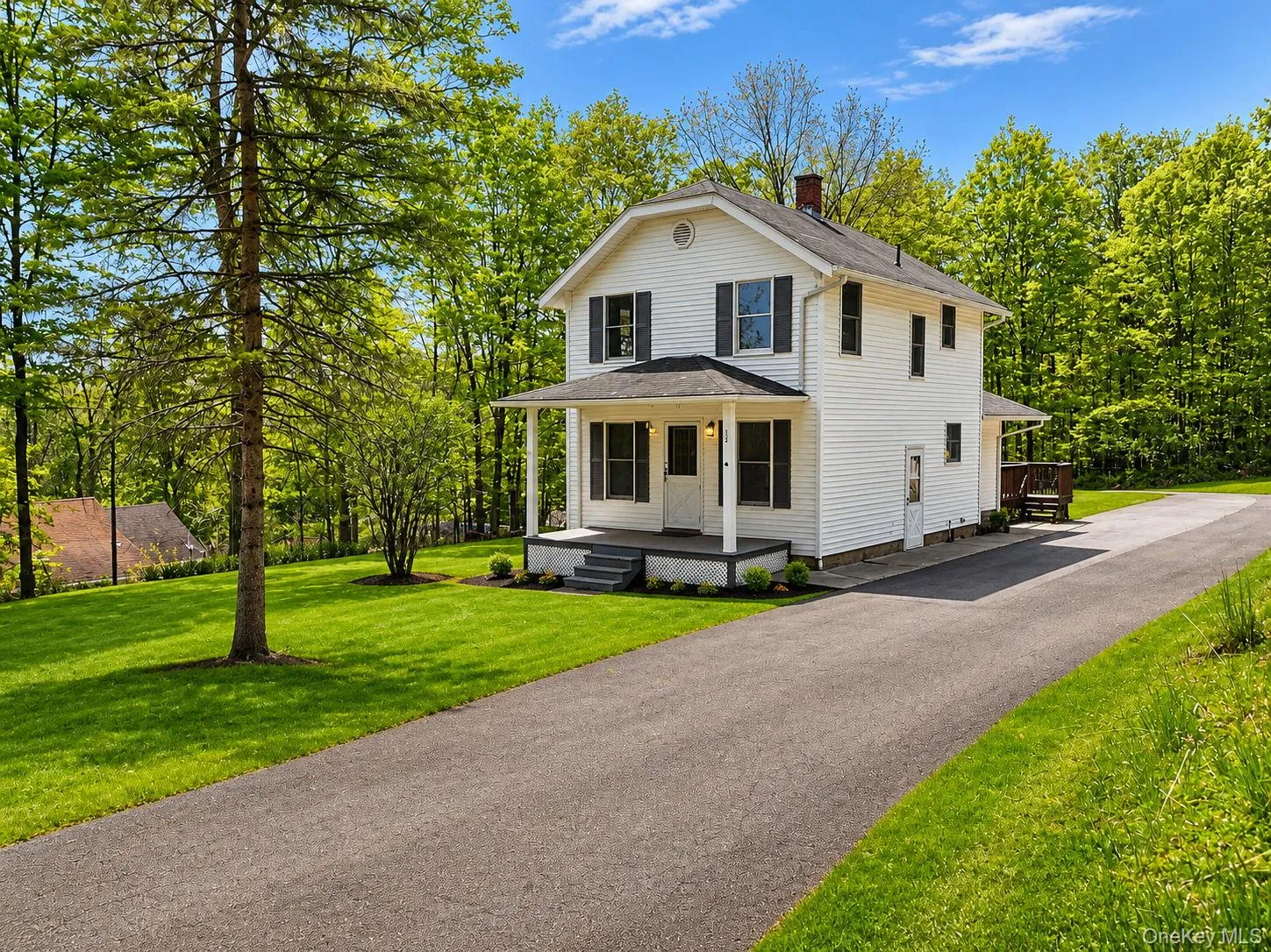White two-story residence with a covered front porch, dark-colored shutters, and a prominent asphalt driveway White two-story residence with a covered front porch, dark-colored shutters, and a prominent asphalt driveway