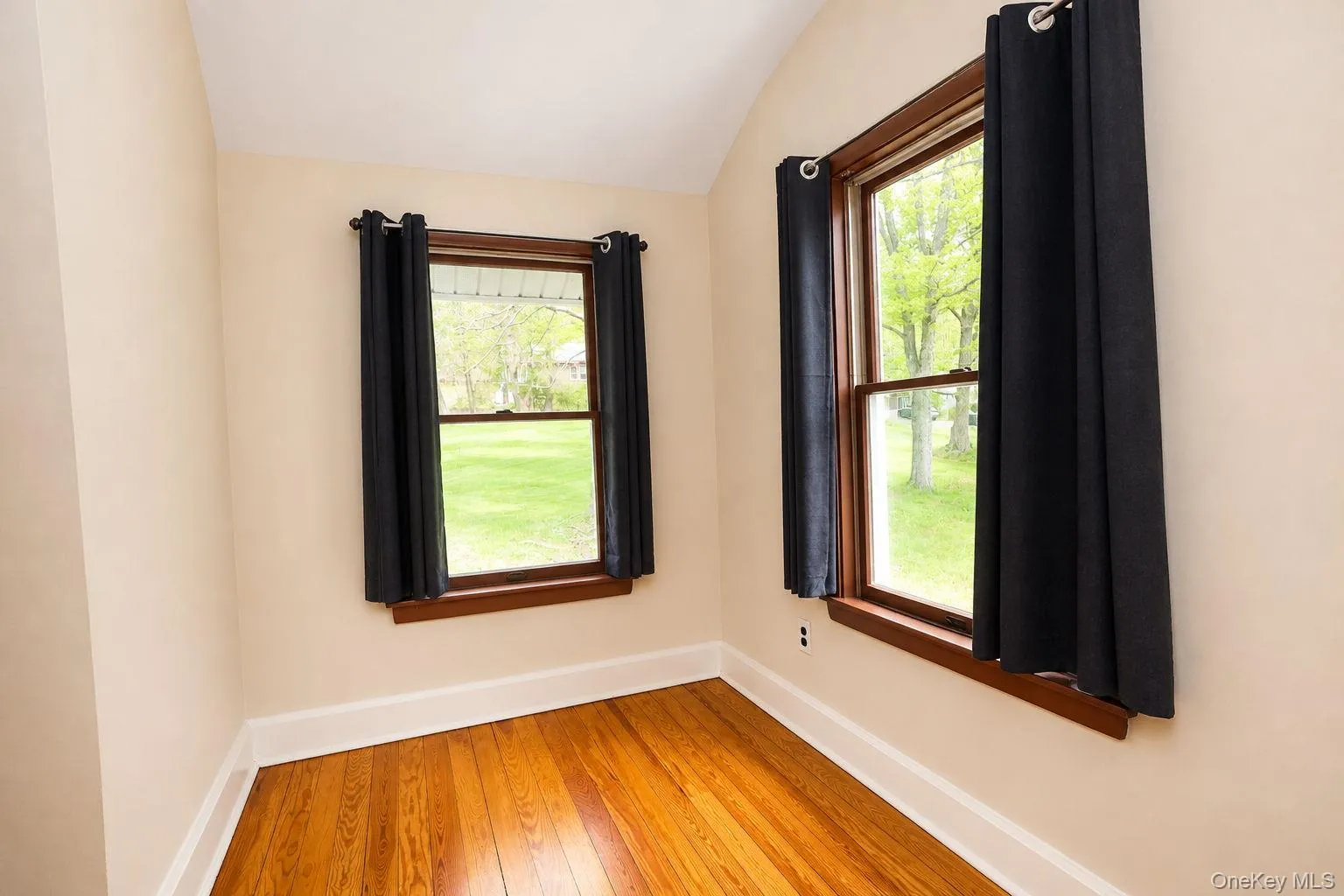 Room with wood-finish flooring, light neutral-toned walls, and white baseboards Room with wood-finish flooring, light neutral-toned walls, and white baseboards