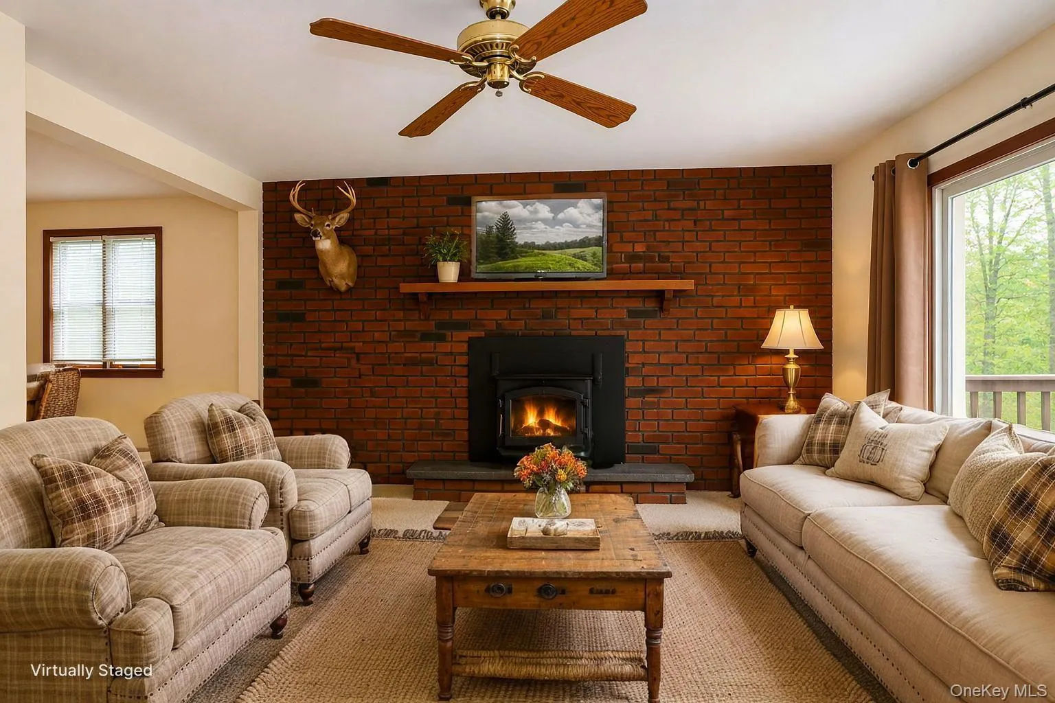 Living space featuring a brick accent wall with a wood-burning stove on a stone hearth, a wood mantel, and wood-finish ceiling fan Living space featuring a brick accent wall with a wood-burning stove on a stone hearth, a wood mantel, and wood-finish ceiling fan