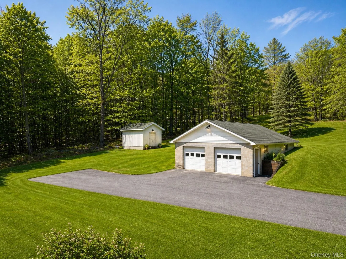Two-car garage with stone facade and white overhead doors, accompanied by a separate storage shed Two-car garage with stone facade and white overhead doors, accompanied by a separate storage shed