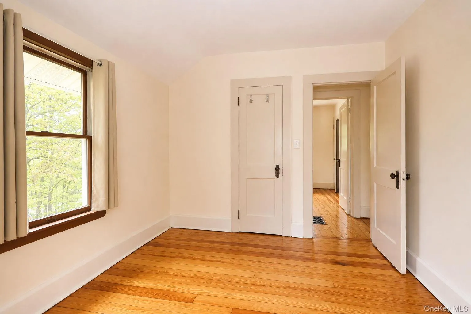 Hardwood flooring throughout this room featuring a window with wood trim, a white door with black hardware, and an additional white door with black hardware Hardwood flooring throughout this room featuring a window with wood trim, a white door with black hardware, and an additional white door with black hardware