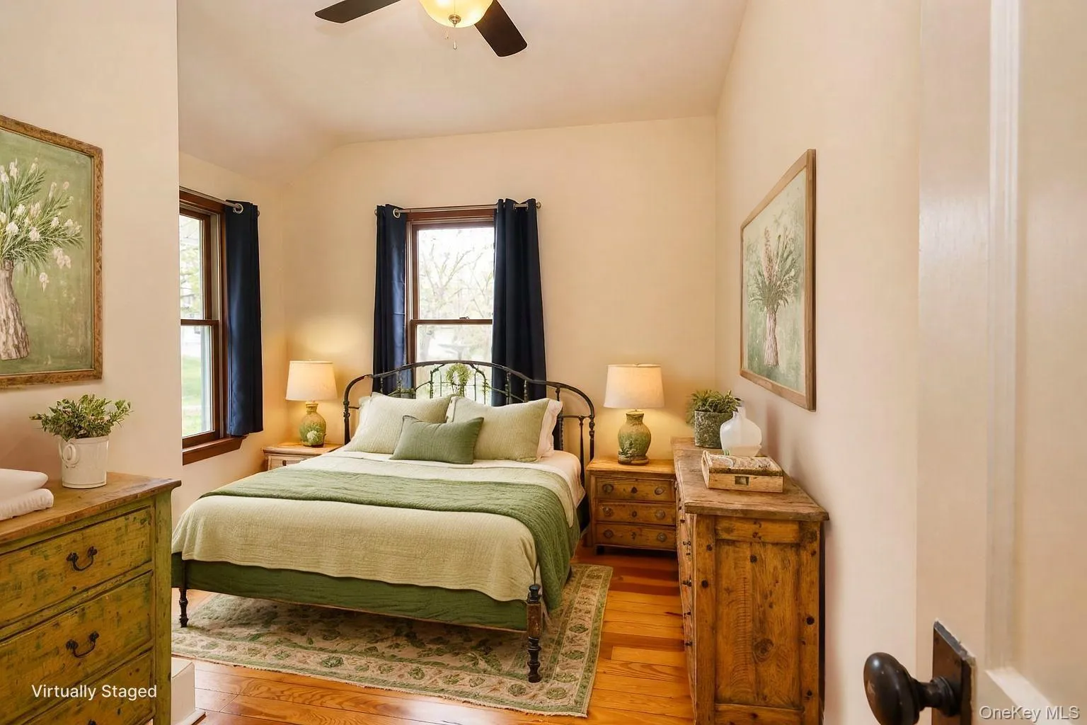 Bedroom featuring hardwood flooring, dual windows with dark drapery, a ceiling fan with integrated lighting, and neutral wall tones Bedroom featuring hardwood flooring, dual windows with dark drapery, a ceiling fan with integrated lighting, and neutral wall tones