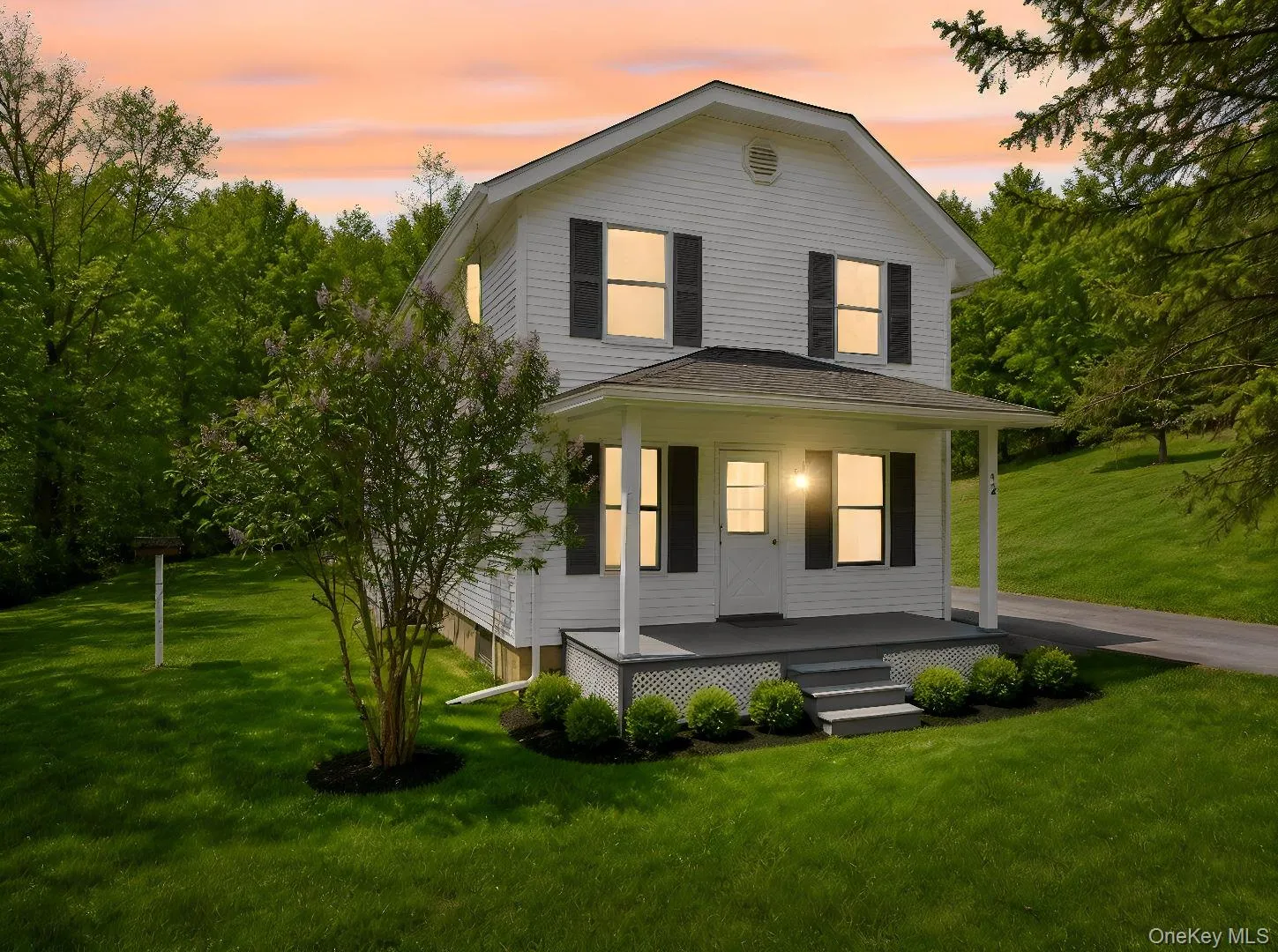 Two-story white residence featuring a front porch with lattice detailing, dark shutters, and a manicured lawn Two-story white residence featuring a front porch with lattice detailing, dark shutters, and a manicured lawn
