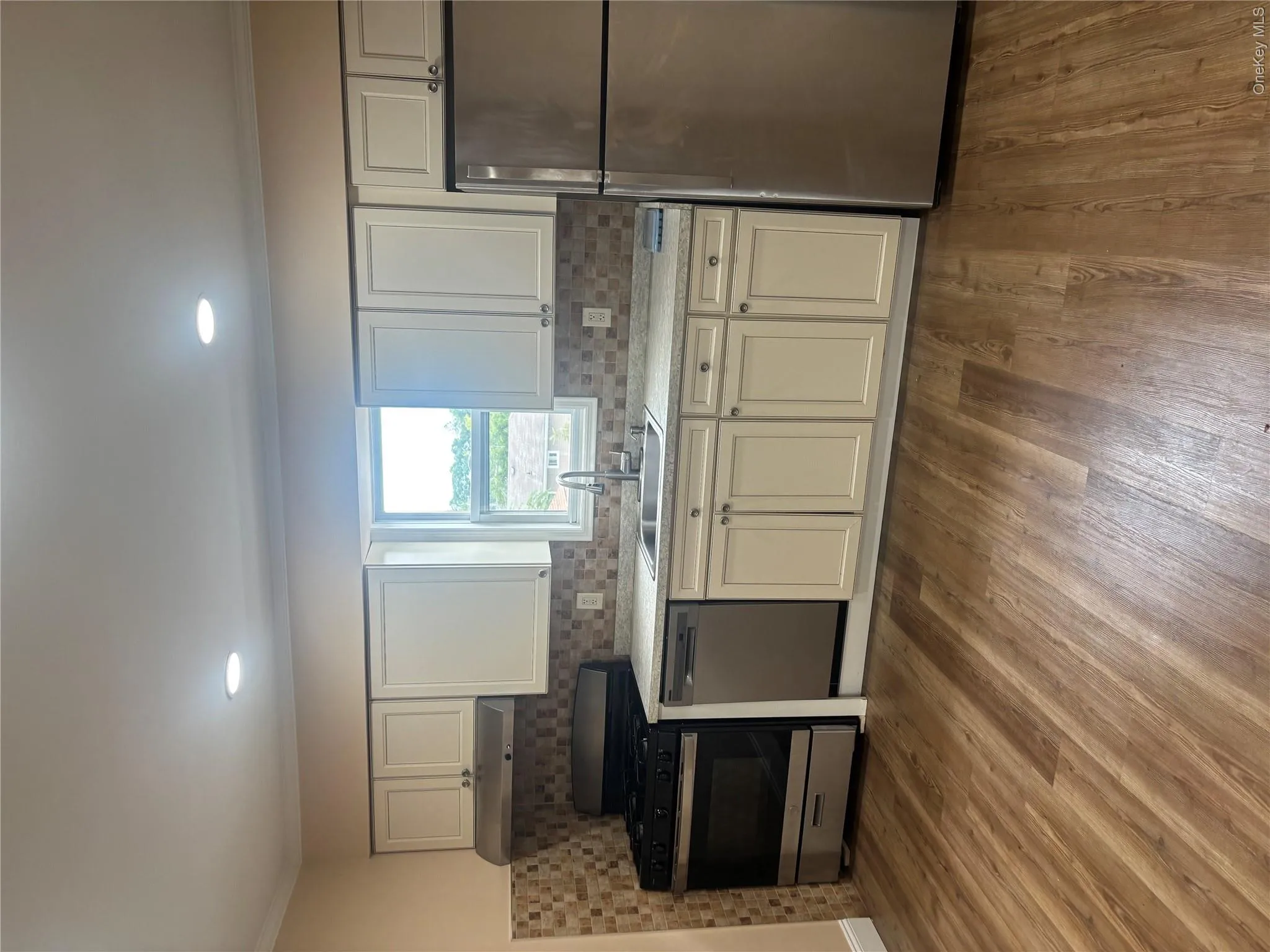 Kitchen featuring wood-finish flooring, recessed lighting, stainless steel appliances, and a tiled backsplash Kitchen featuring wood-finish flooring, recessed lighting, stainless steel appliances, and a tiled backsplash