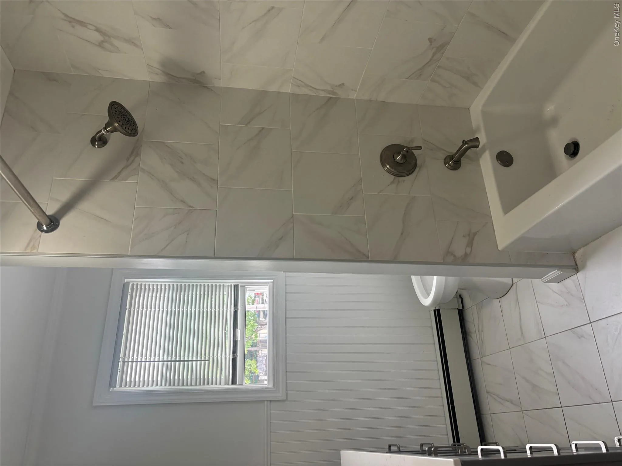 White tiled tub surround, modern shower head, white bathtub, white floor tiles, and white beadboard paneling White tiled tub surround, modern shower head, white bathtub, white floor tiles, and white beadboard paneling
