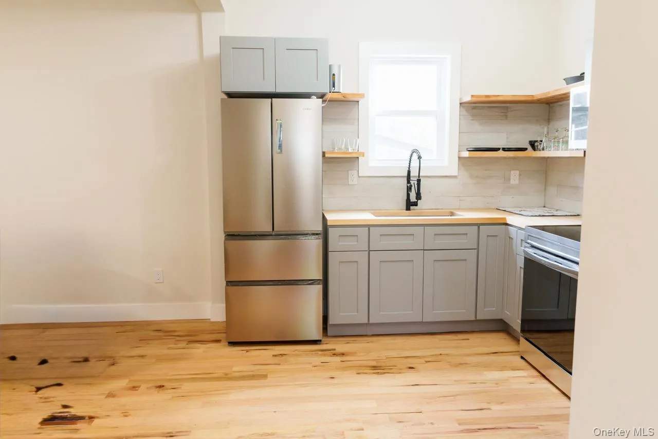Kitchen with open shelves, stainless steel appliances, gray cabinets, and light countertops Kitchen with open shelves, stainless steel appliances, gray cabinets, and light countertops