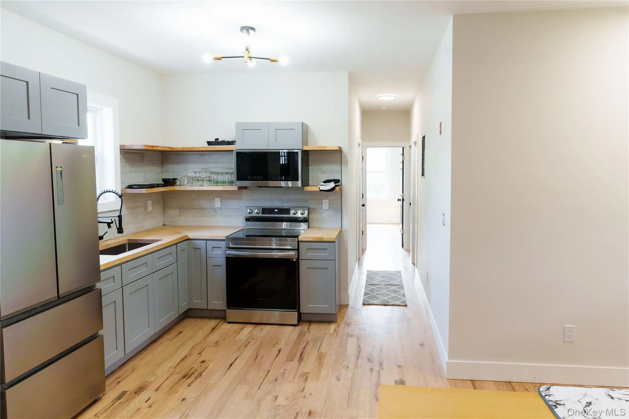 Kitchen featuring gray cabinets, appliances with stainless steel finishes, open shelves, backsplash, and light wood finished floors Kitchen featuring gray cabinets, appliances with stainless steel finishes, open shelves, backsplash, and light wood finished floors