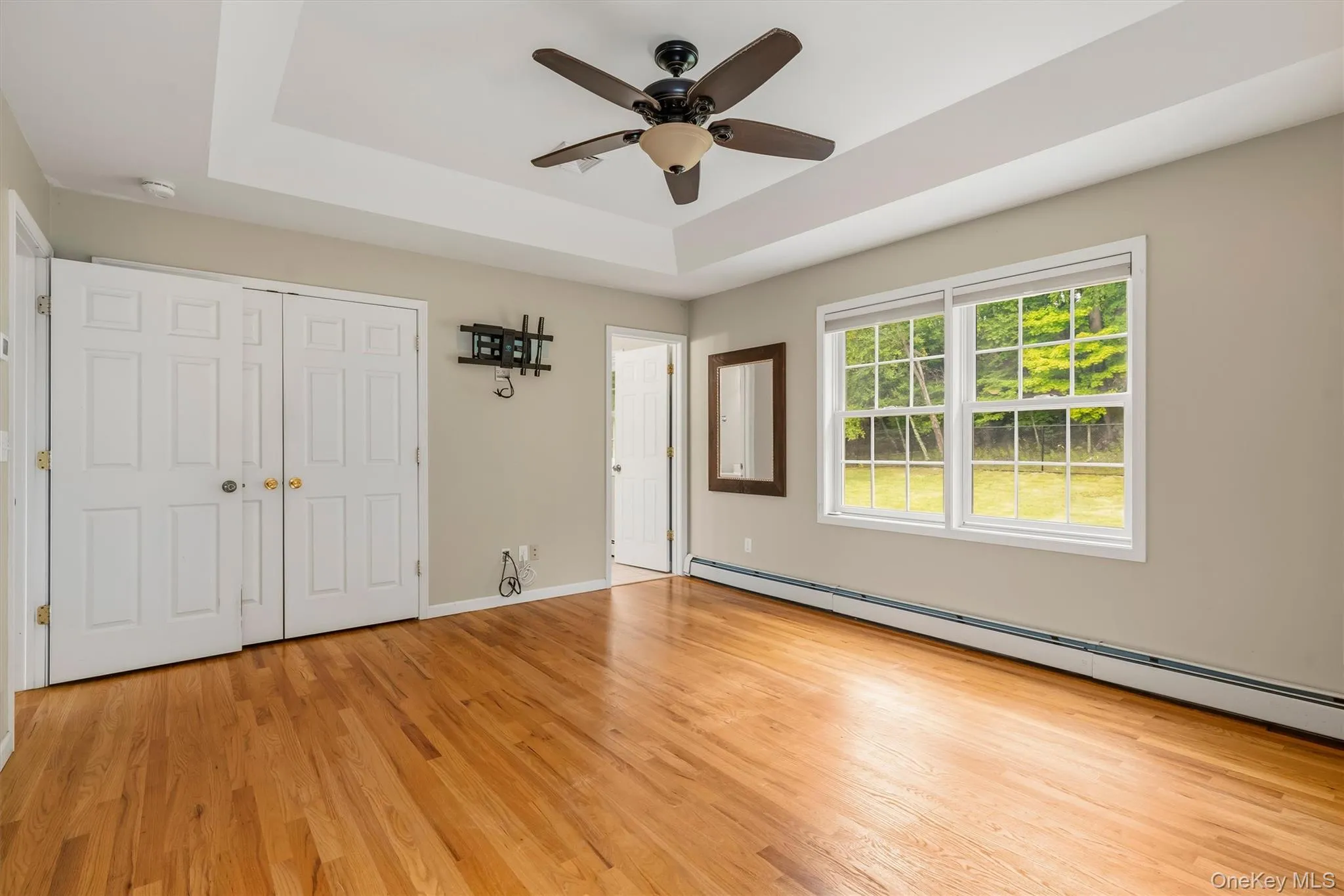 Tray ceiling with a ceiling fan, wood-finish flooring, and white double-pane windows Tray ceiling with a ceiling fan, wood-finish flooring, and white double-pane windows
