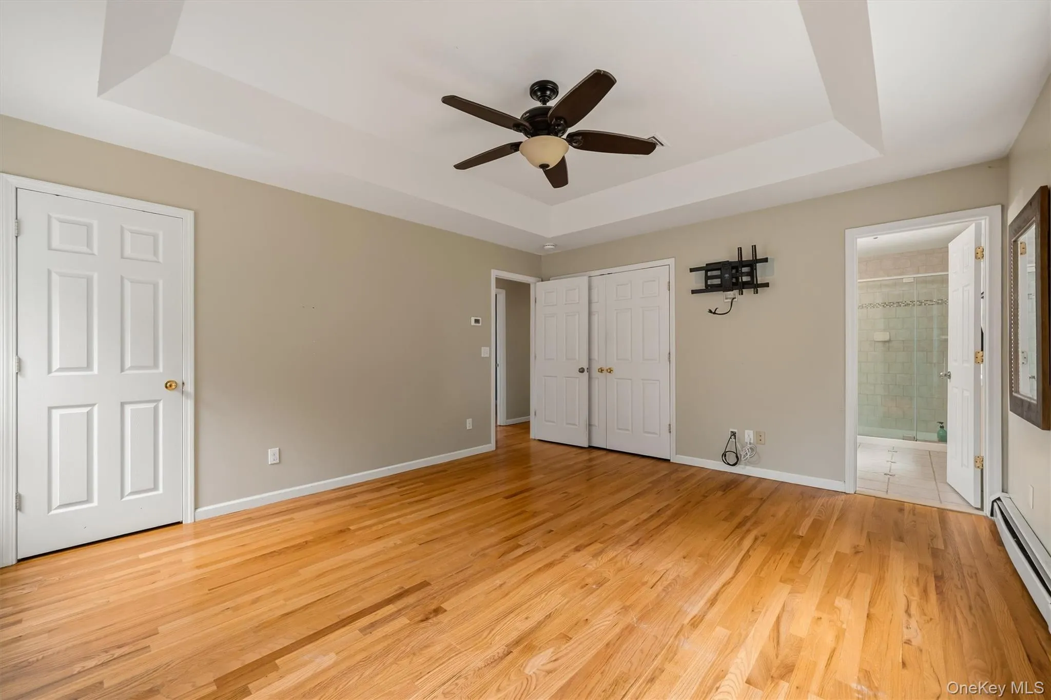 Wood-finish flooring, tray ceiling, ceiling fan, and white paneled doors Wood-finish flooring, tray ceiling, ceiling fan, and white paneled doors