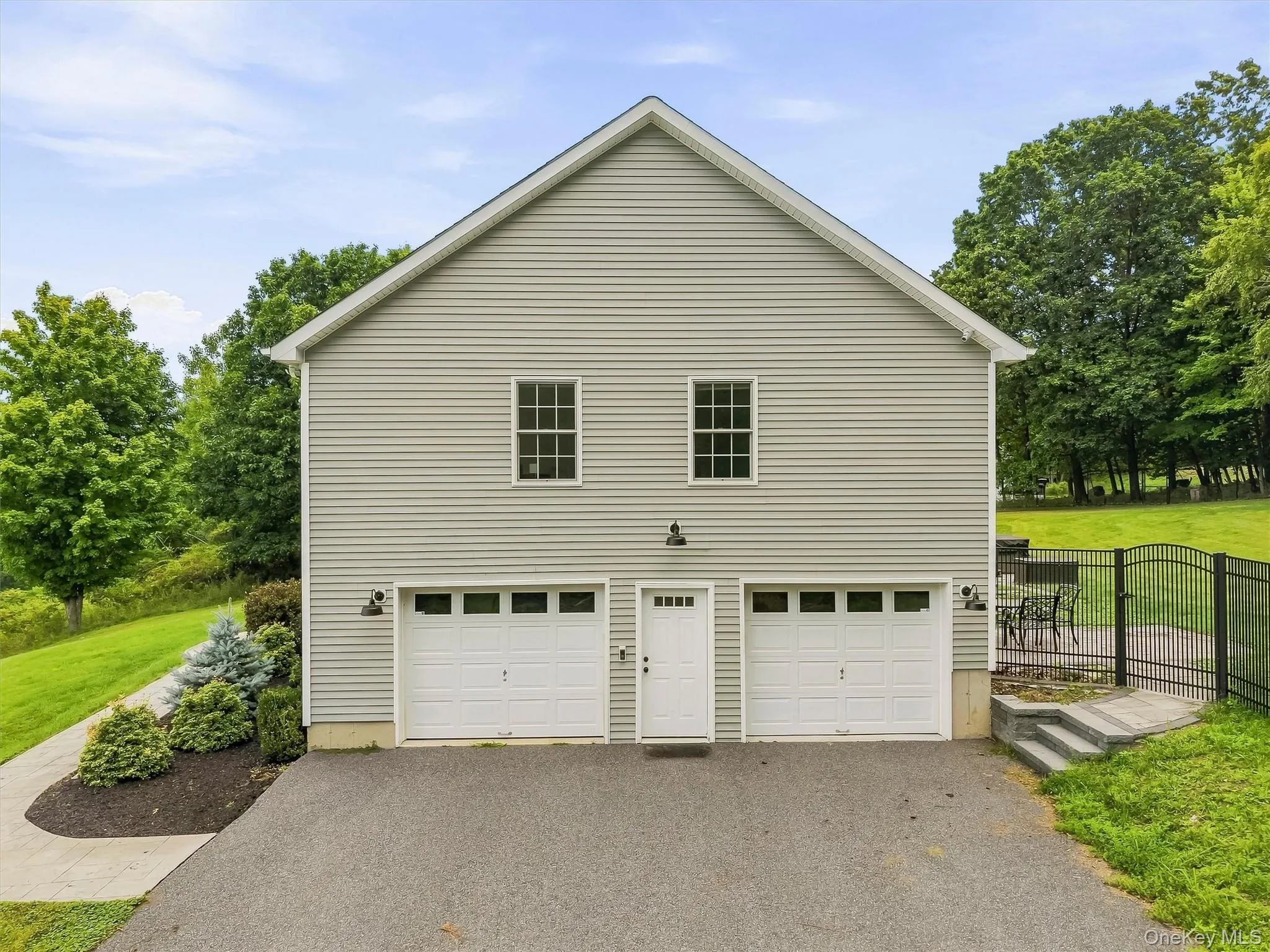 Two-story exterior with horizontal siding, featuring two garage doors, a pedestrian entrance, and a wrought iron fence with gate Two-story exterior with horizontal siding, featuring two garage doors, a pedestrian entrance, and a wrought iron fence with gate