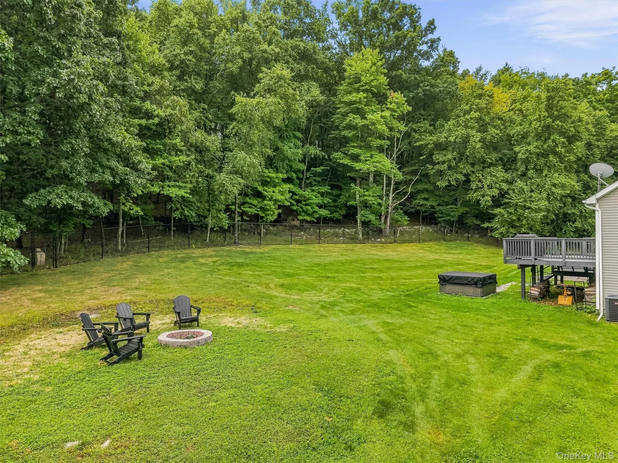 Expansive lawn area with a built-in fire pit, privacy fencing, and mature trees bordering the property Expansive lawn area with a built-in fire pit, privacy fencing, and mature trees bordering the property