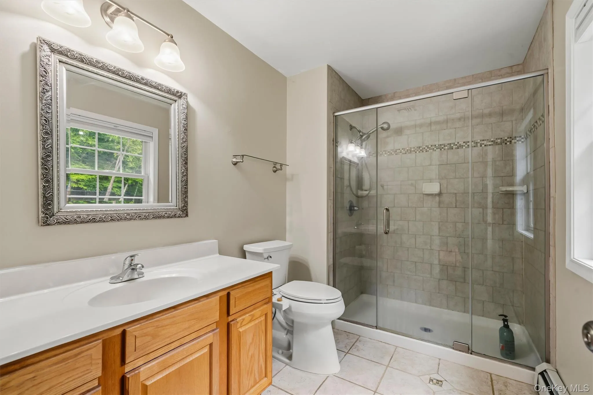 Tile flooring, wood-finish vanity with an integrated sink and chrome faucet, framed mirror, and a glass-enclosed shower with tiled walls Tile flooring, wood-finish vanity with an integrated sink and chrome faucet, framed mirror, and a glass-enclosed shower with tiled walls