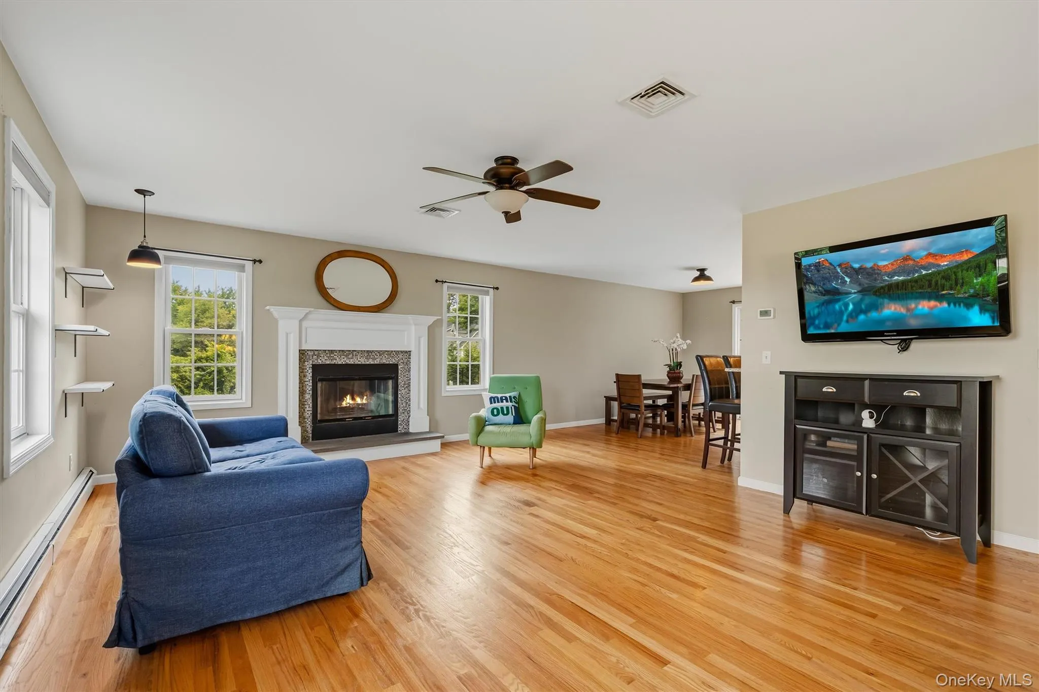 Hardwood flooring throughout, a white fireplace with a tile surround and mantel, built-in shelving, a ceiling fan, and recessed lighting Hardwood flooring throughout, a white fireplace with a tile surround and mantel, built-in shelving, a ceiling fan, and recessed lighting