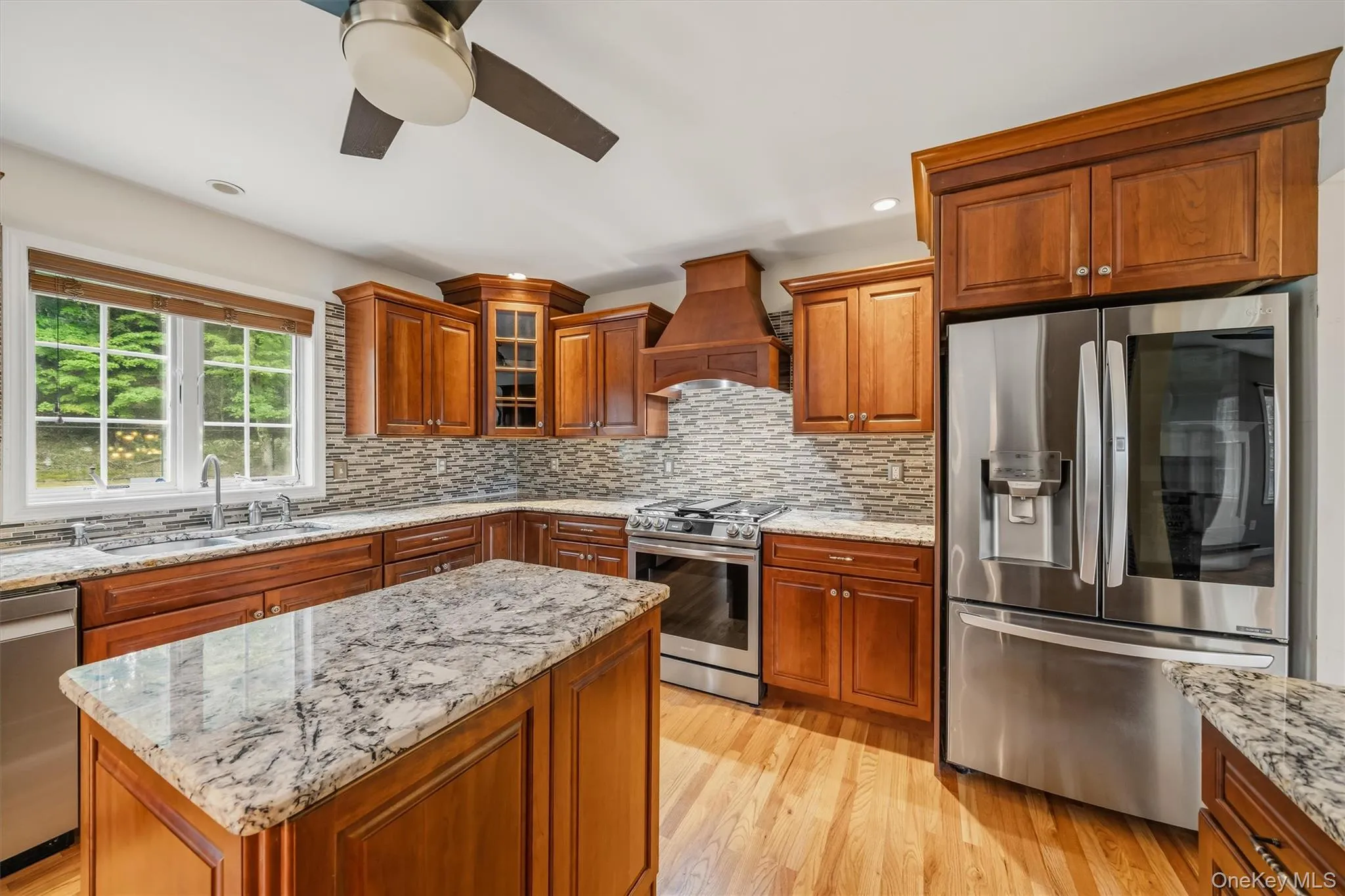 Gourmet kitchen featuring wood cabinetry, stainless steel appliances, a tile backsplash, and light-toned wood flooring Gourmet kitchen featuring wood cabinetry, stainless steel appliances, a tile backsplash, and light-toned wood flooring