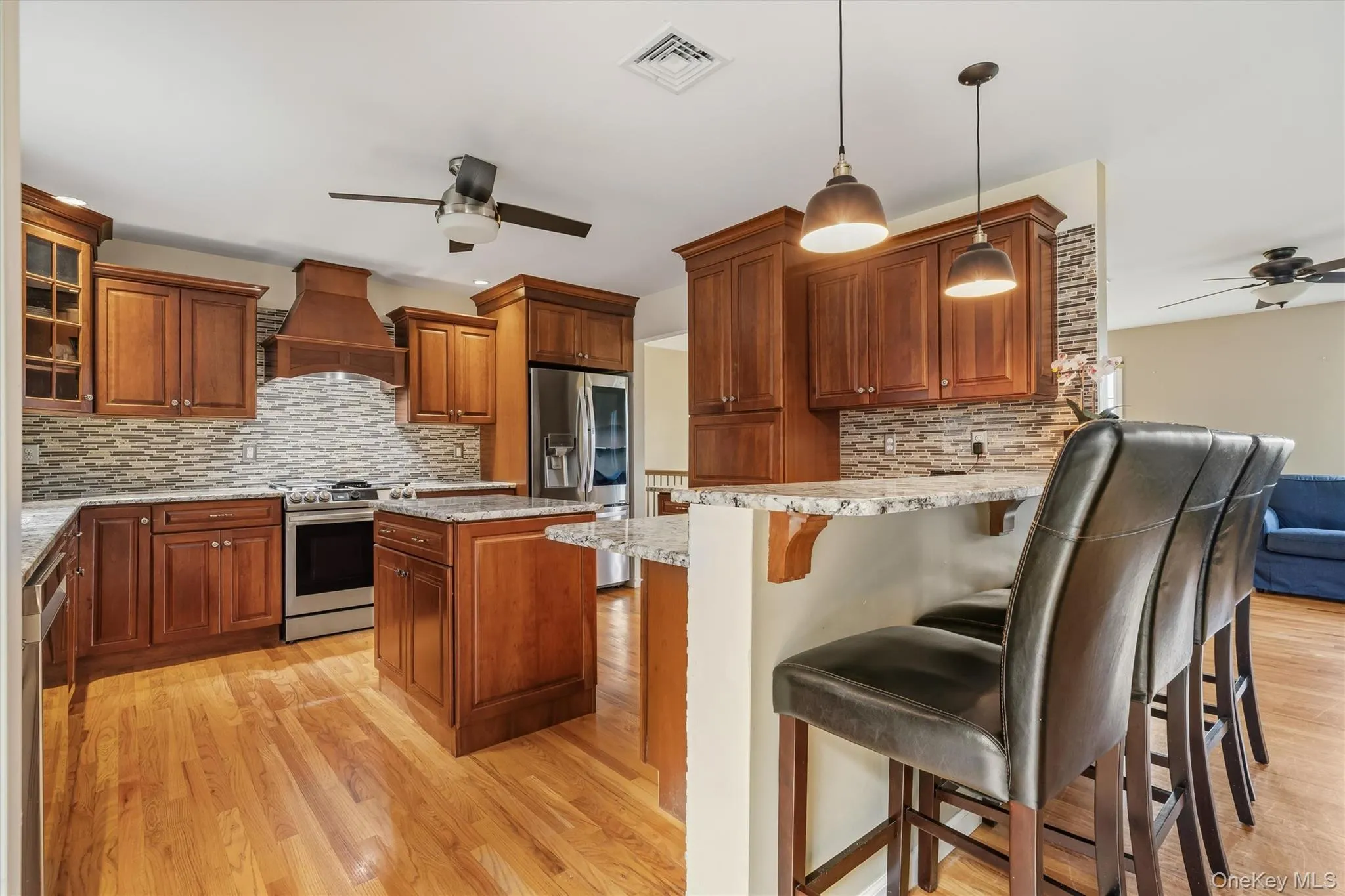 Wood-finish cabinetry, stainless steel appliances, natural wood-finish flooring, stone-finish countertops, and a stone-finish backsplash Wood-finish cabinetry, stainless steel appliances, natural wood-finish flooring, stone-finish countertops, and a stone-finish backsplash