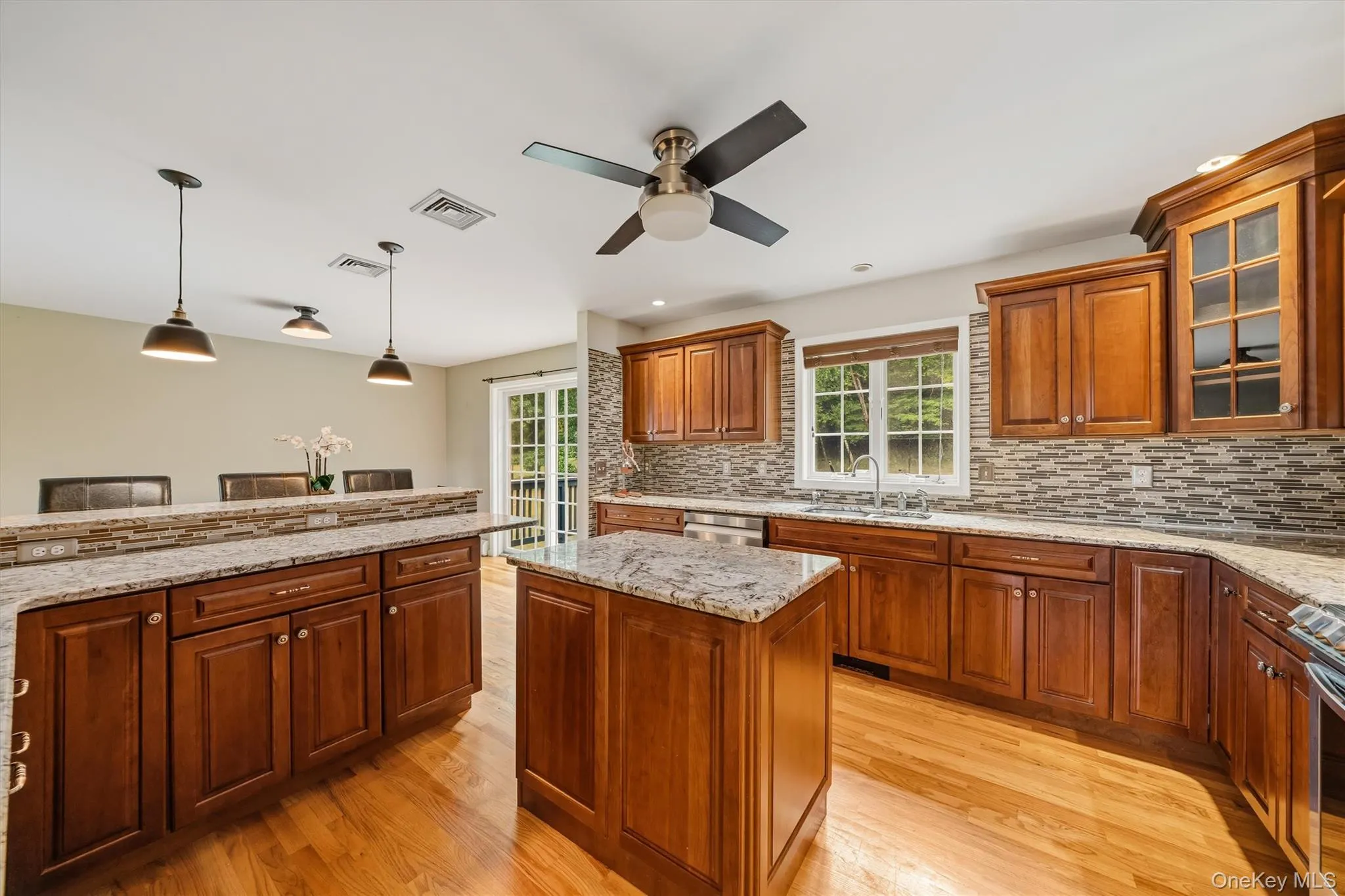 Hardwood flooring, wood cabinetry, granite countertops, stone tile backsplash, and a central kitchen island Hardwood flooring, wood cabinetry, granite countertops, stone tile backsplash, and a central kitchen island
