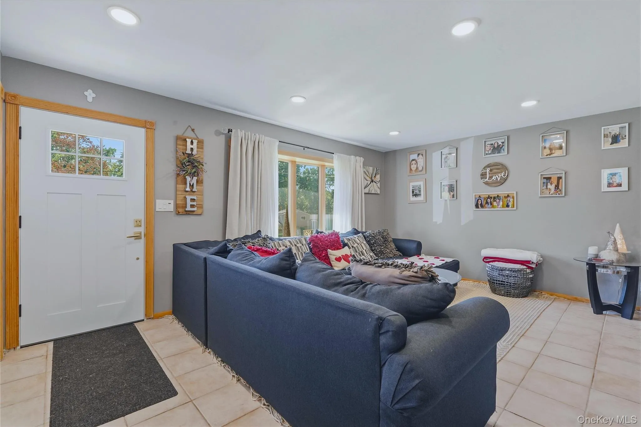 Your new living room with recessed ceiling lighting, tiled flooring, front entry door with transom window, and a large window with natural light Your new living room with recessed ceiling lighting, tiled flooring, front entry door with transom window, and a large window with natural light