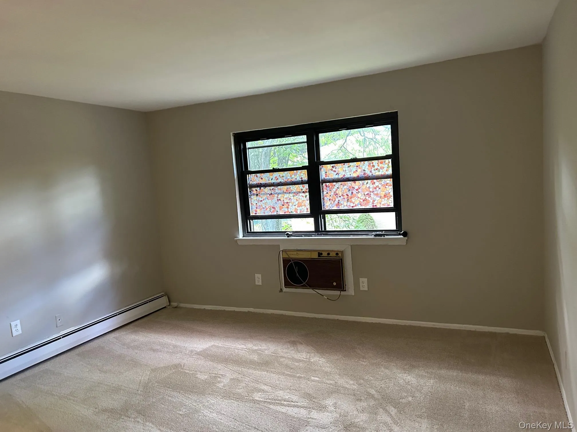 Empty room with light carpet, baseboard heating, and a wall unit AC Empty room with light carpet, baseboard heating, and a wall unit AC