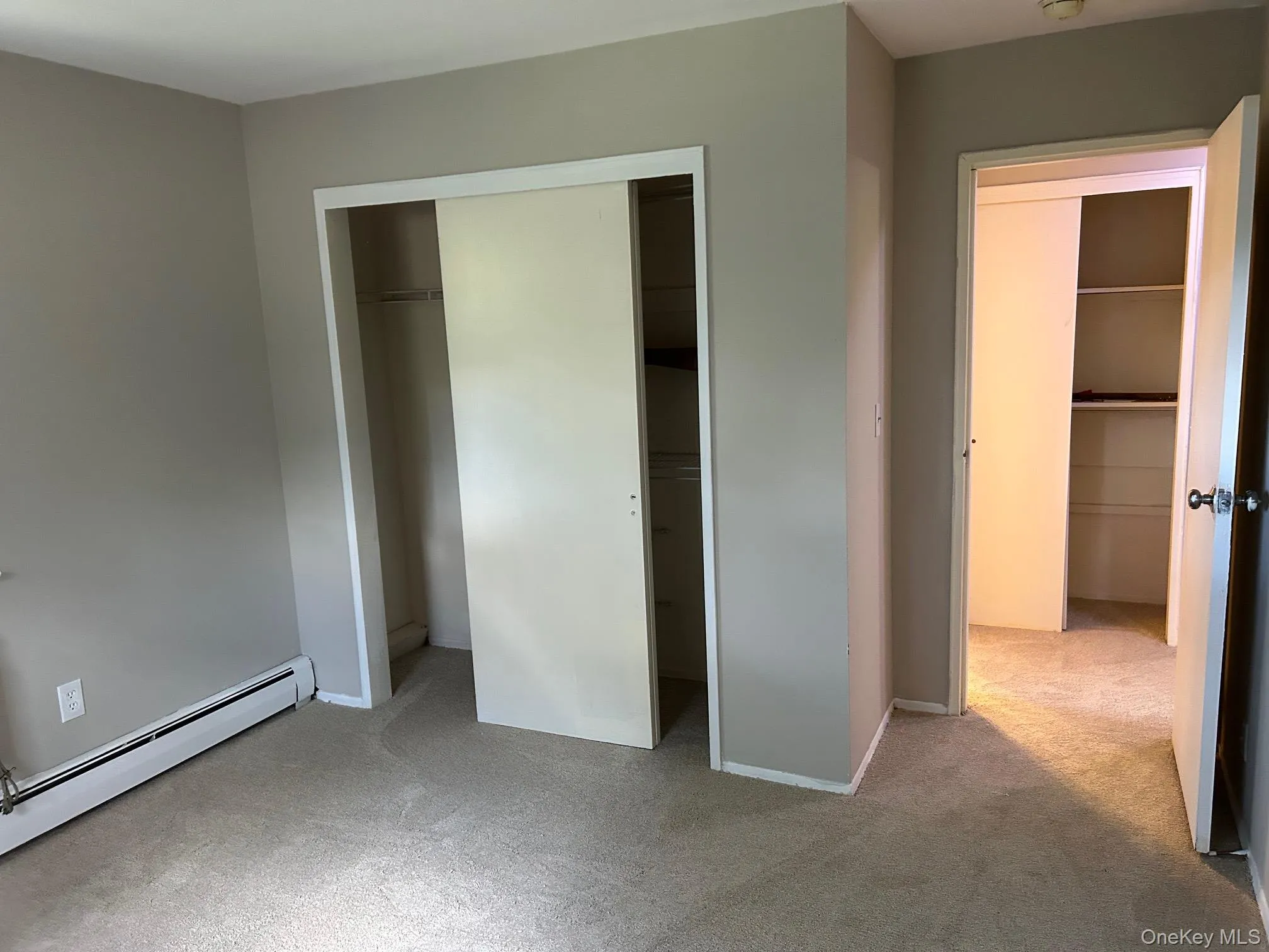 Unfurnished bedroom with light colored carpet, a closet, and baseboard heating Unfurnished bedroom with light colored carpet, a closet, and baseboard heating