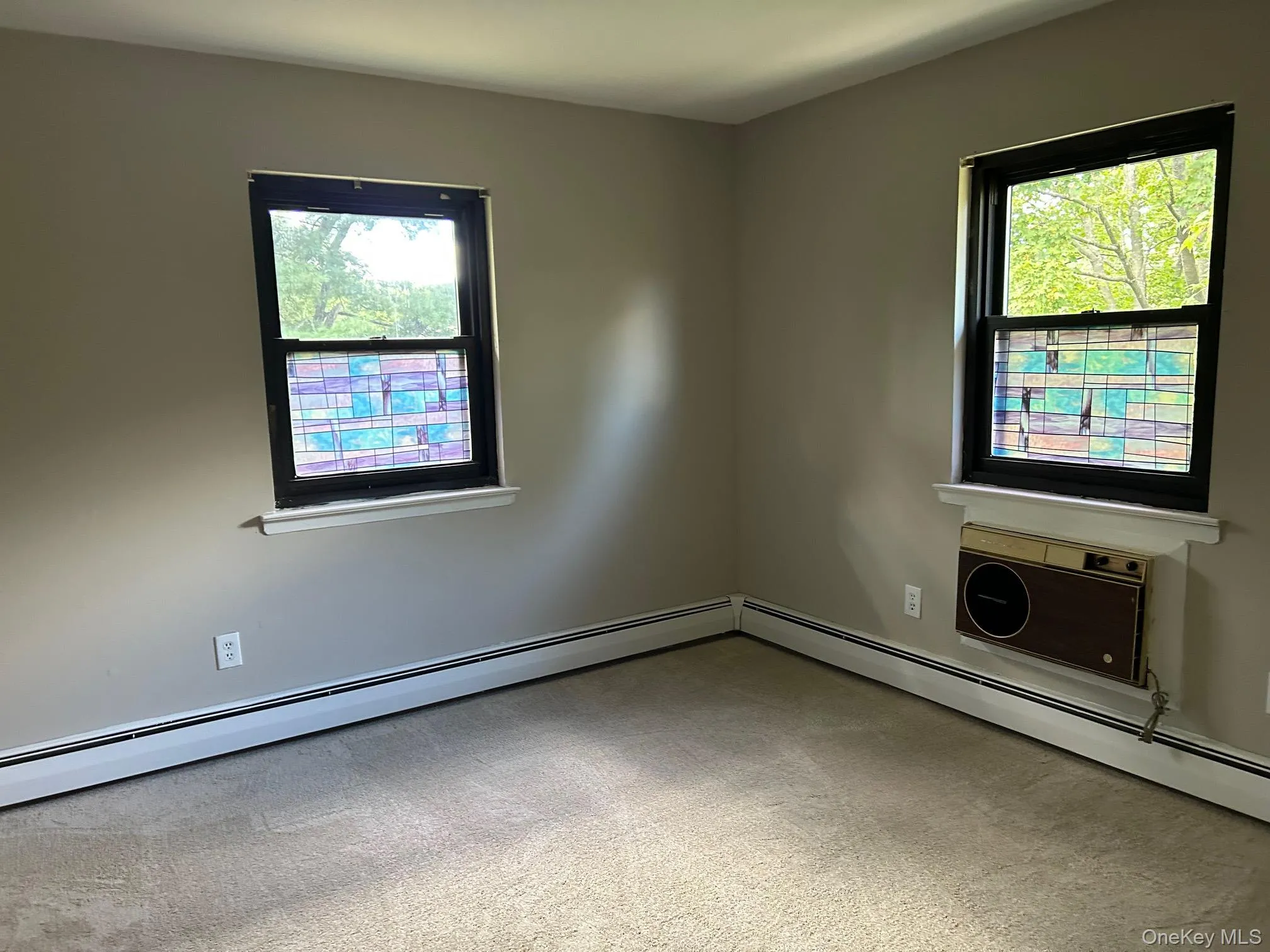 Unfurnished room featuring light colored carpet, baseboard heating, and a wall mounted AC Unfurnished room featuring light colored carpet, baseboard heating, and a wall mounted AC
