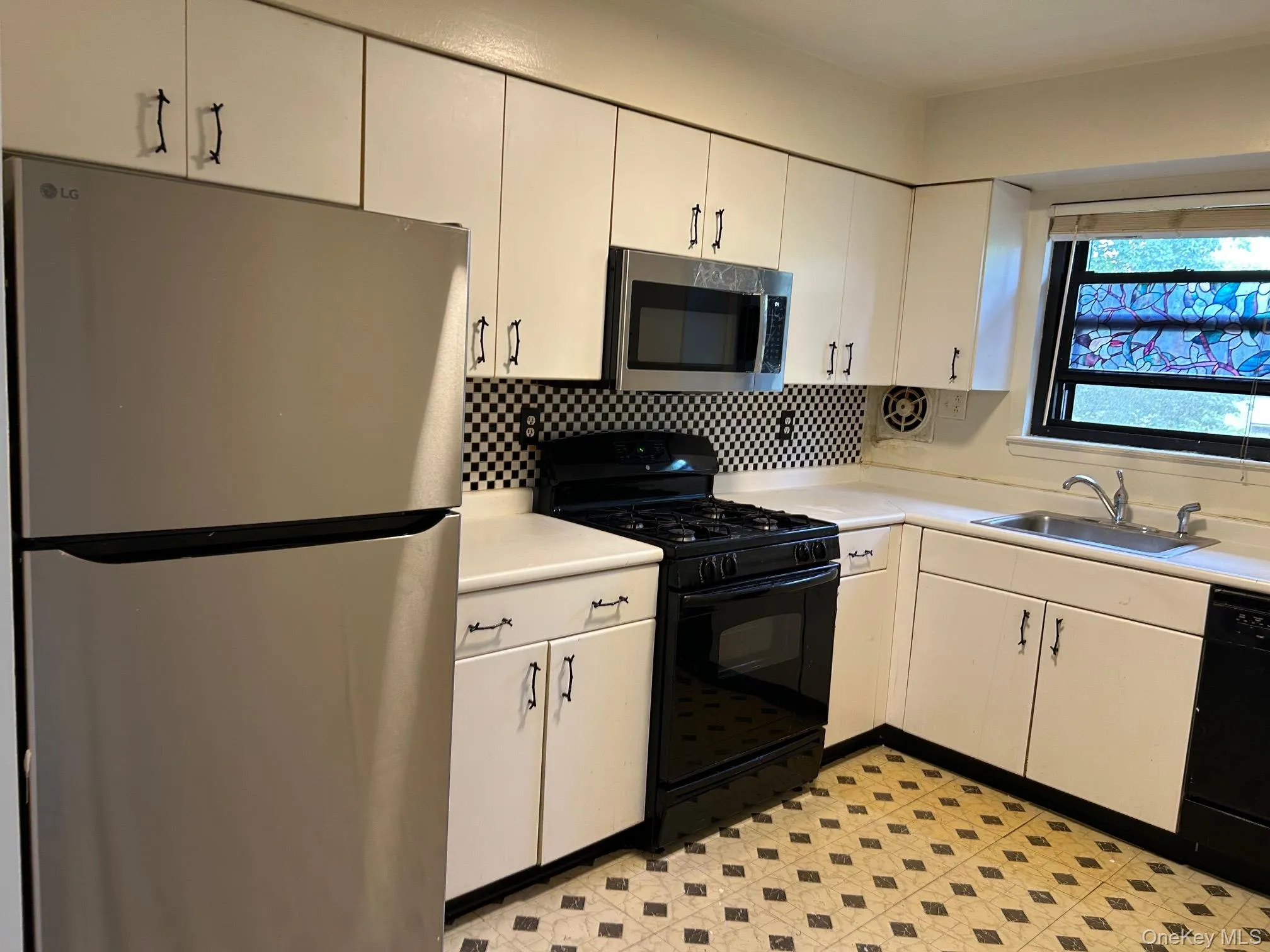 Kitchen with black appliances, light countertops, light flooring, and white cabinetry Kitchen with black appliances, light countertops, light flooring, and white cabinetry