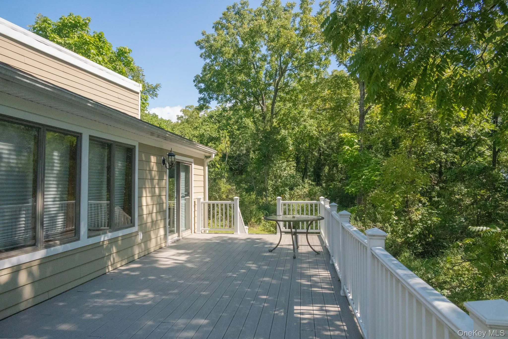 Spacious exterior deck with white railing, wood-finish decking, and direct outdoor access via a glass-paneled door Spacious exterior deck with white railing, wood-finish decking, and direct outdoor access via a glass-paneled door
