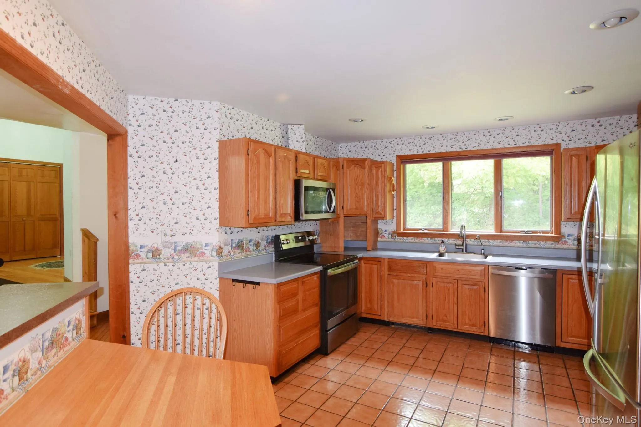 Kitchen featuring wood cabinetry, tile flooring, stainless steel appliances, and a window above the sink Kitchen featuring wood cabinetry, tile flooring, stainless steel appliances, and a window above the sink