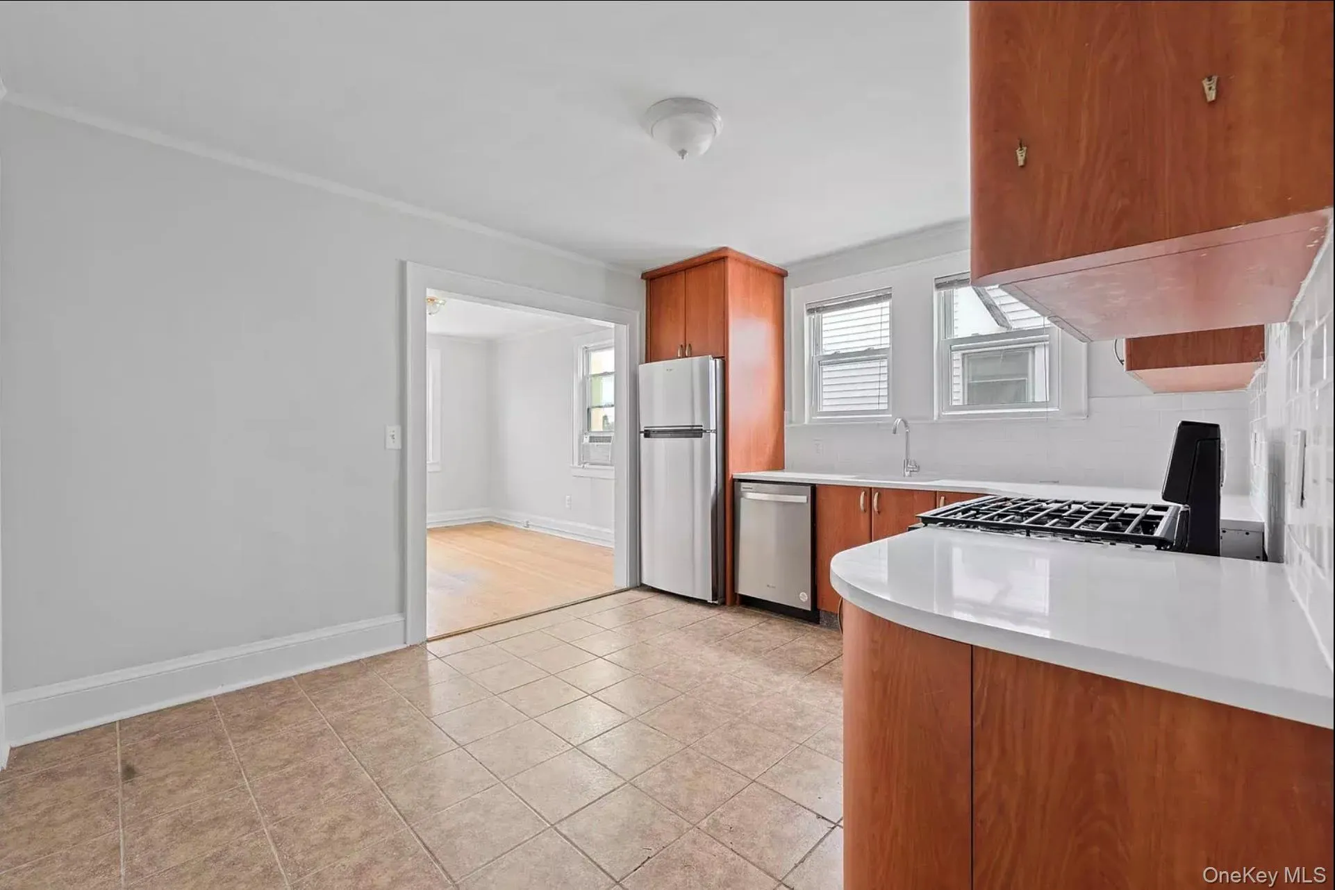 Kitchen featuring stainless steel appliances, light countertops, brown cabinetry, light tile patterned flooring, and a sink Kitchen featuring stainless steel appliances, light countertops, brown cabinetry, light tile patterned flooring, and a sink