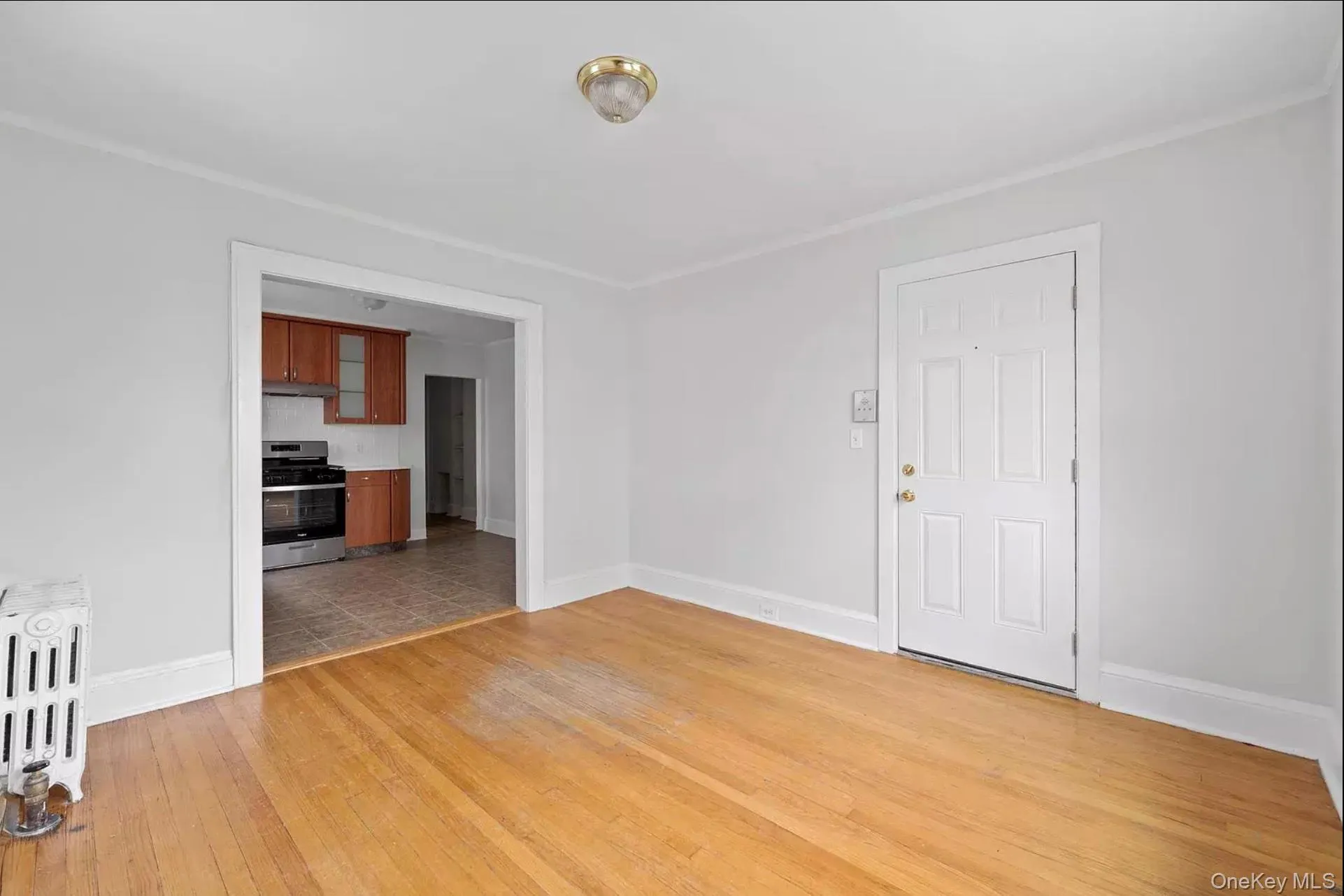 Unfurnished living room with radiator, light wood-style floors, and baseboards Unfurnished living room with radiator, light wood-style floors, and baseboards