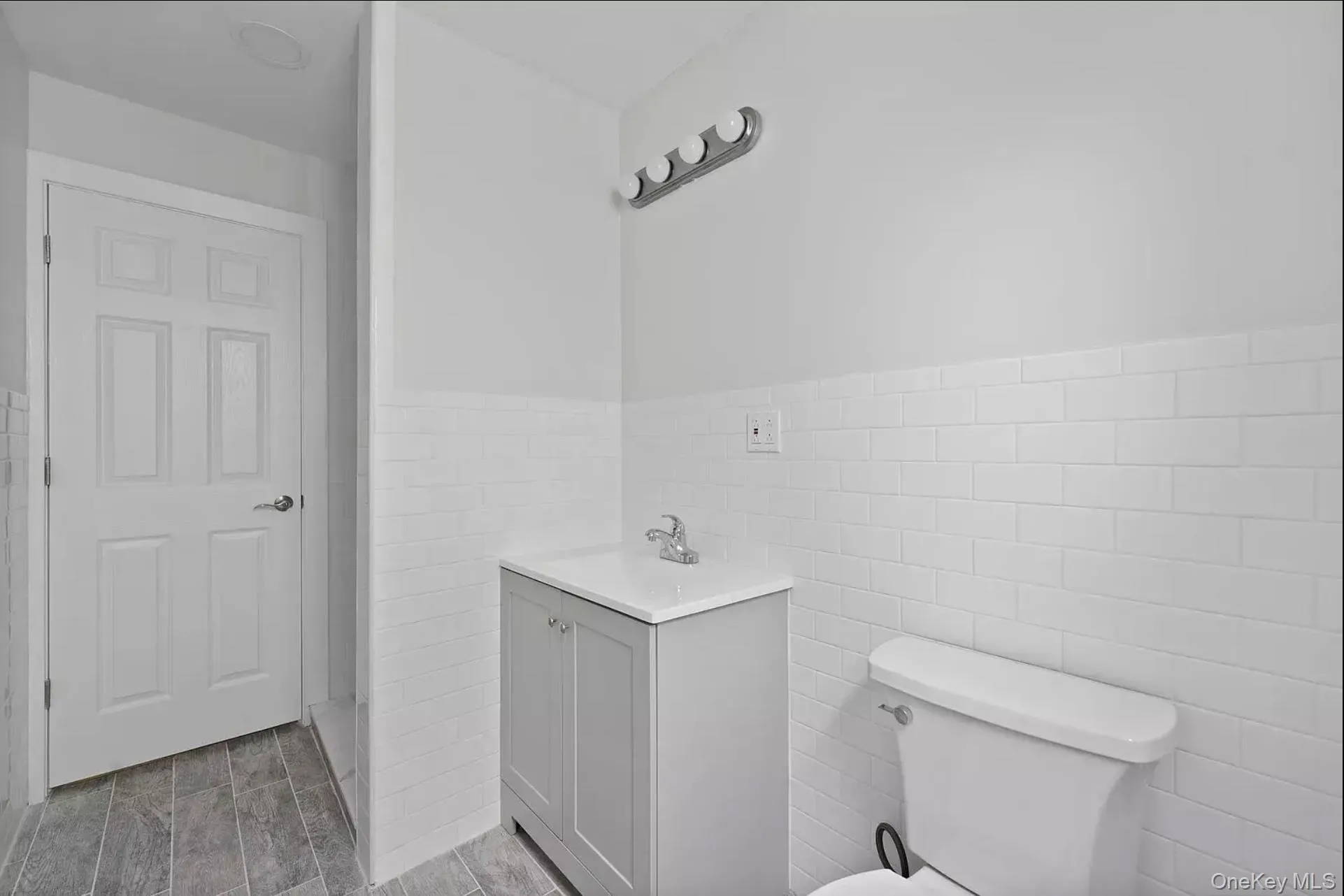 Bathroom with tile walls, vanity, toilet, and a wainscoted wall Bathroom with tile walls, vanity, toilet, and a wainscoted wall