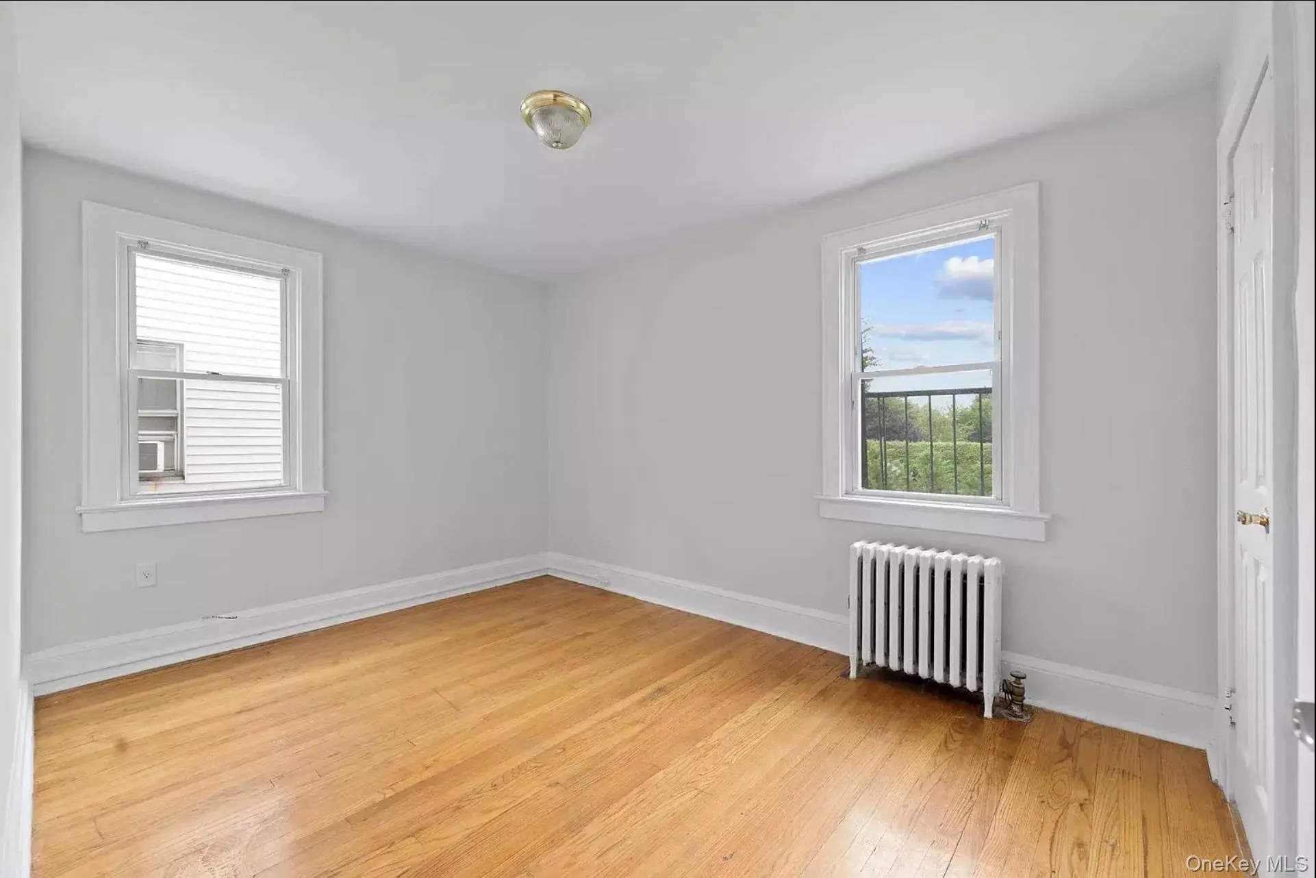 Empty room with radiator heating unit, light wood finished floors, and baseboards Empty room with radiator heating unit, light wood finished floors, and baseboards