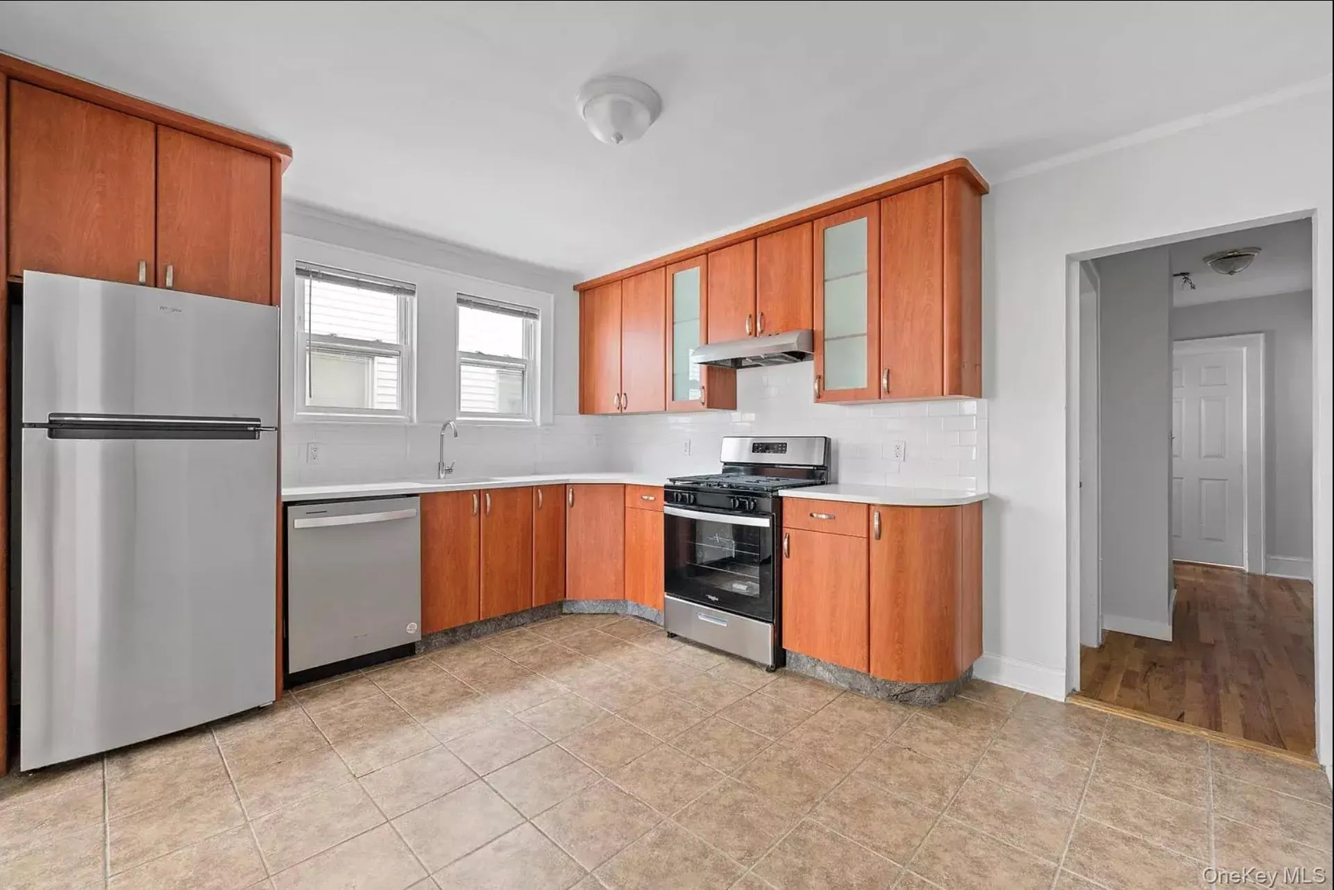 Kitchen featuring appliances with stainless steel finishes, under cabinet range hood, light countertops, backsplash, and glass insert cabinets Kitchen featuring appliances with stainless steel finishes, under cabinet range hood, light countertops, backsplash, and glass insert cabinets