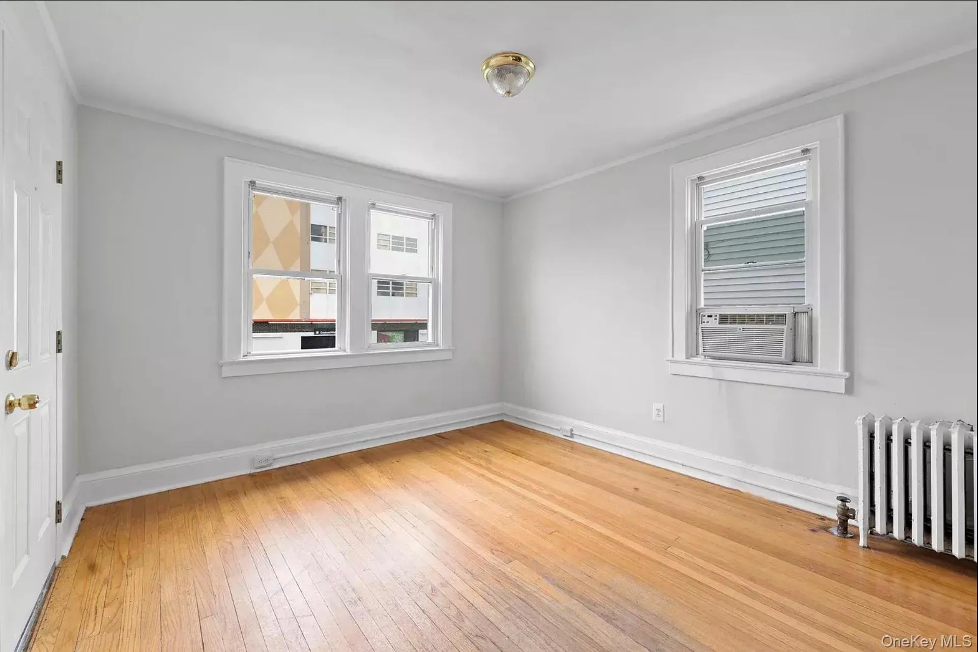 Spare room featuring radiator heating unit, cooling unit, ornamental molding, light wood-style floors, and baseboards Spare room featuring radiator heating unit, cooling unit, ornamental molding, light wood-style floors, and baseboards