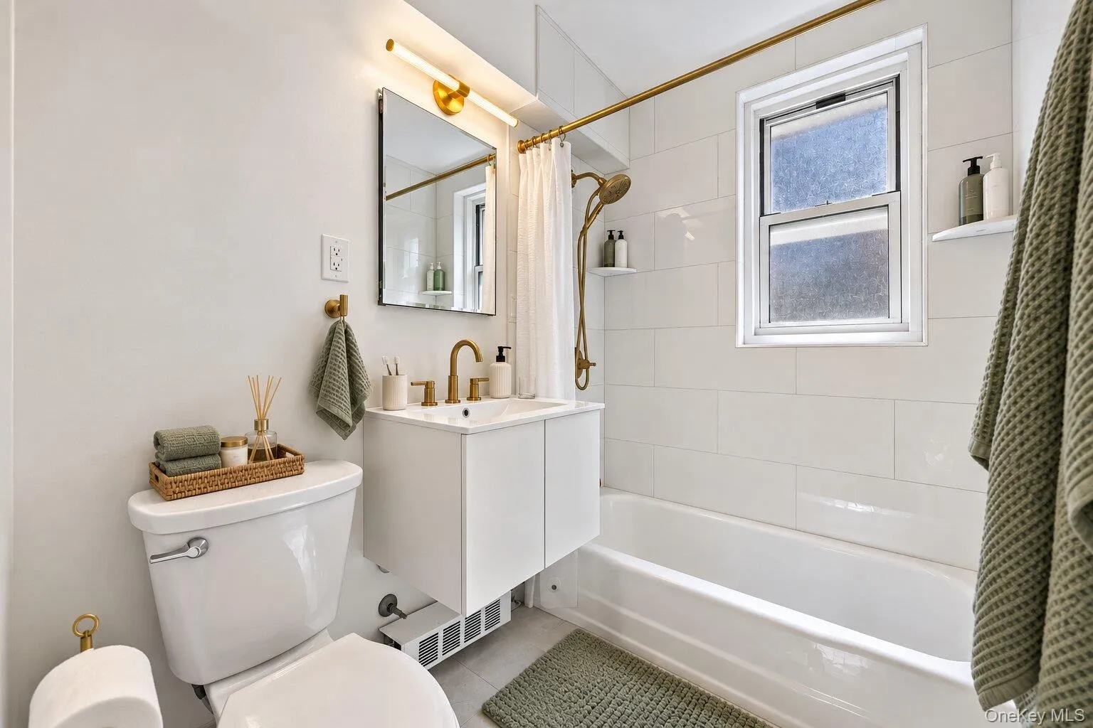 White subway tile tub surround, gold-finish fixtures, white wall-mounted vanity, and a window with privacy glass White subway tile tub surround, gold-finish fixtures, white wall-mounted vanity, and a window with privacy glass