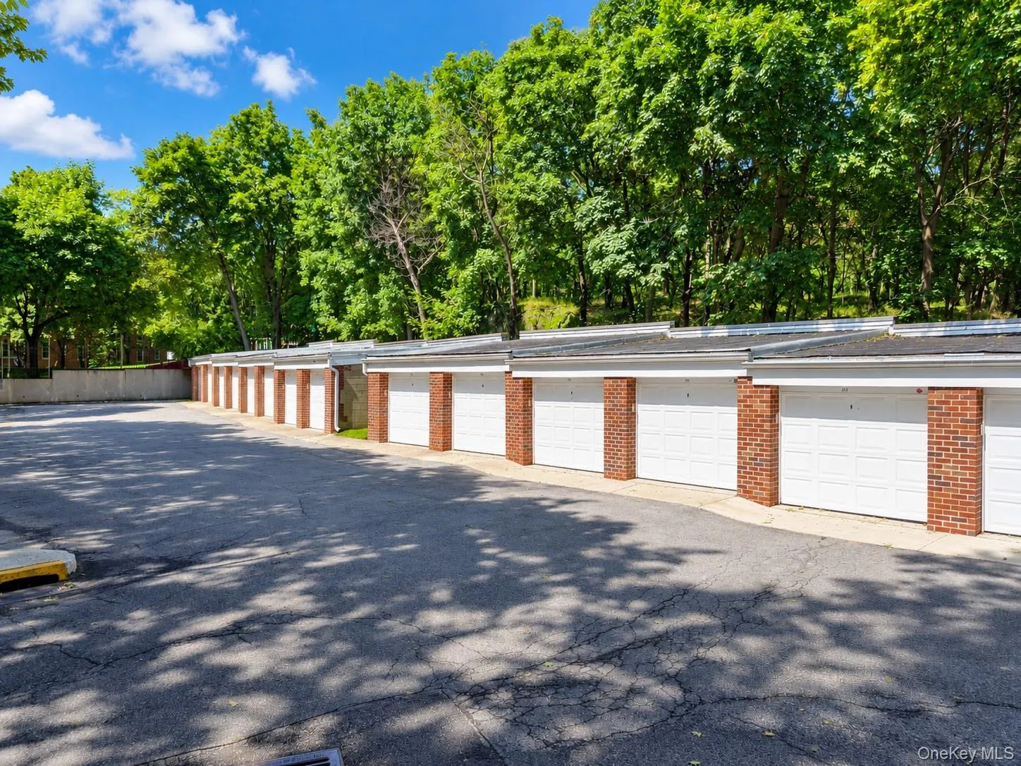 Rows of individual garages with white doors and brick accents, complemented by mature trees in the background Rows of individual garages with white doors and brick accents, complemented by mature trees in the background