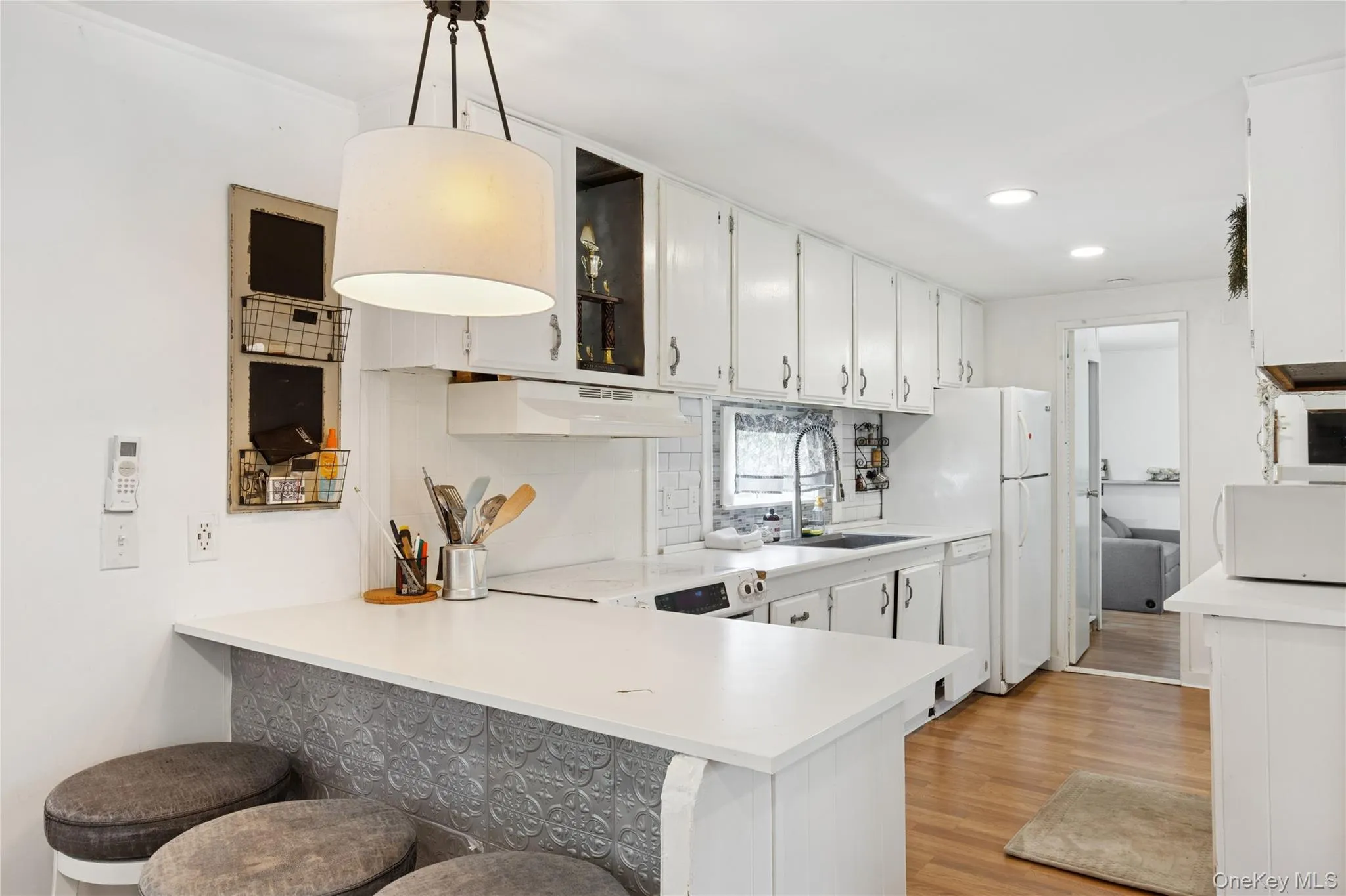 Kitchen featuring decorative backsplash, light countertops, a peninsula, decorative light fixtures, and white cabinetry Kitchen featuring decorative backsplash, light countertops, a peninsula, decorative light fixtures, and white cabinetry