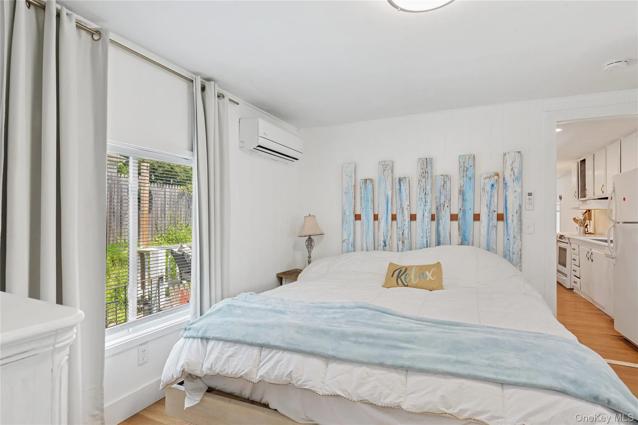 Bedroom featuring light wood-style floors, freestanding refrigerator, and a wall unit AC Bedroom featuring light wood-style floors, freestanding refrigerator, and a wall unit AC