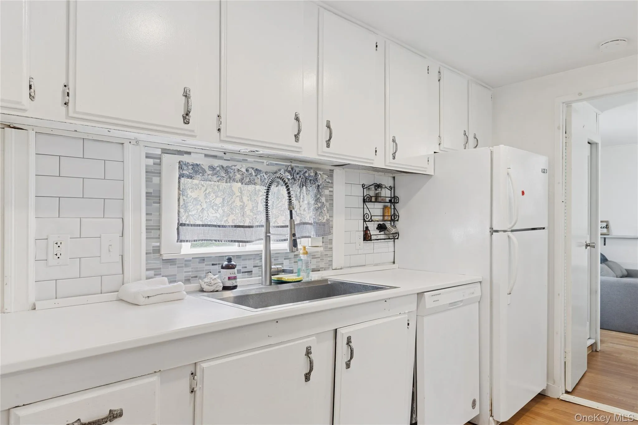 Kitchen with light countertops, decorative backsplash, white cabinetry, and white appliances Kitchen with light countertops, decorative backsplash, white cabinetry, and white appliances