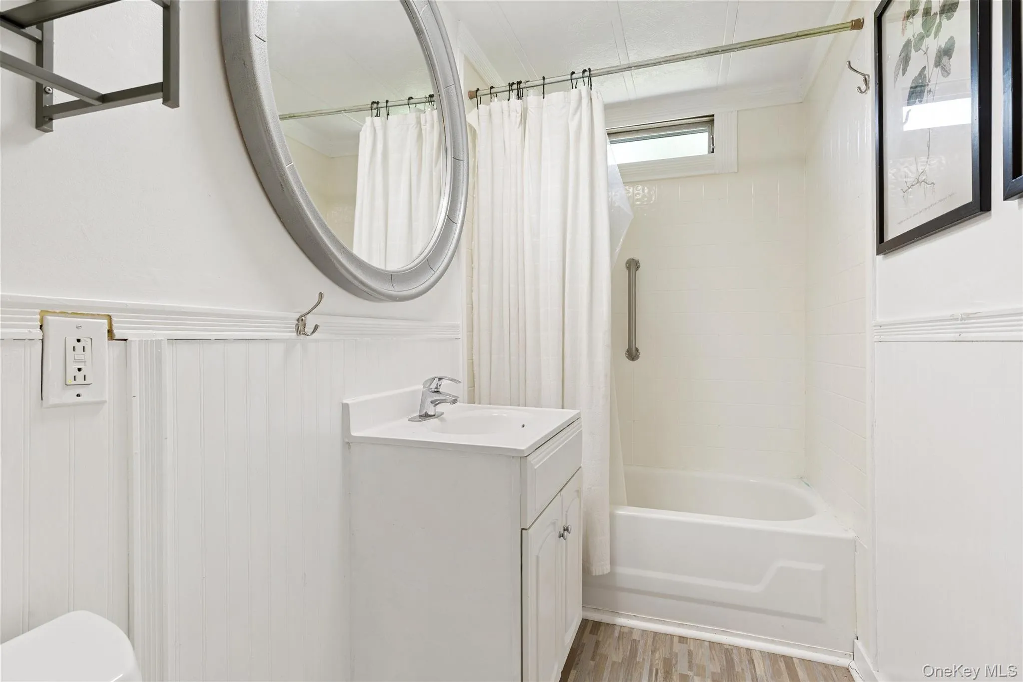 Bathroom with light wood-type flooring, shower / bath combo with shower curtain, vanity, and a wainscoted wall Bathroom with light wood-type flooring, shower / bath combo with shower curtain, vanity, and a wainscoted wall