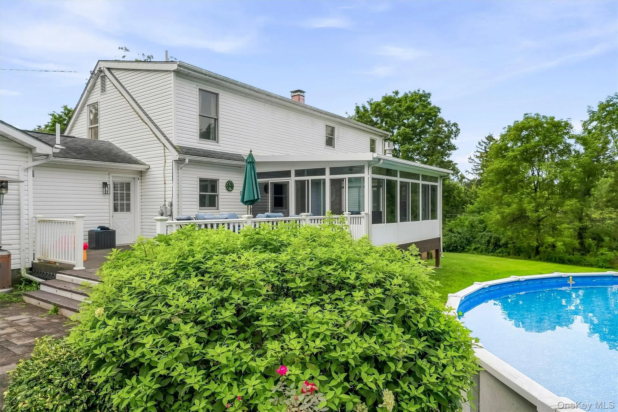 White siding exterior with a multi-level deck, enclosed porch, and an above-ground swimming pool White siding exterior with a multi-level deck, enclosed porch, and an above-ground swimming pool