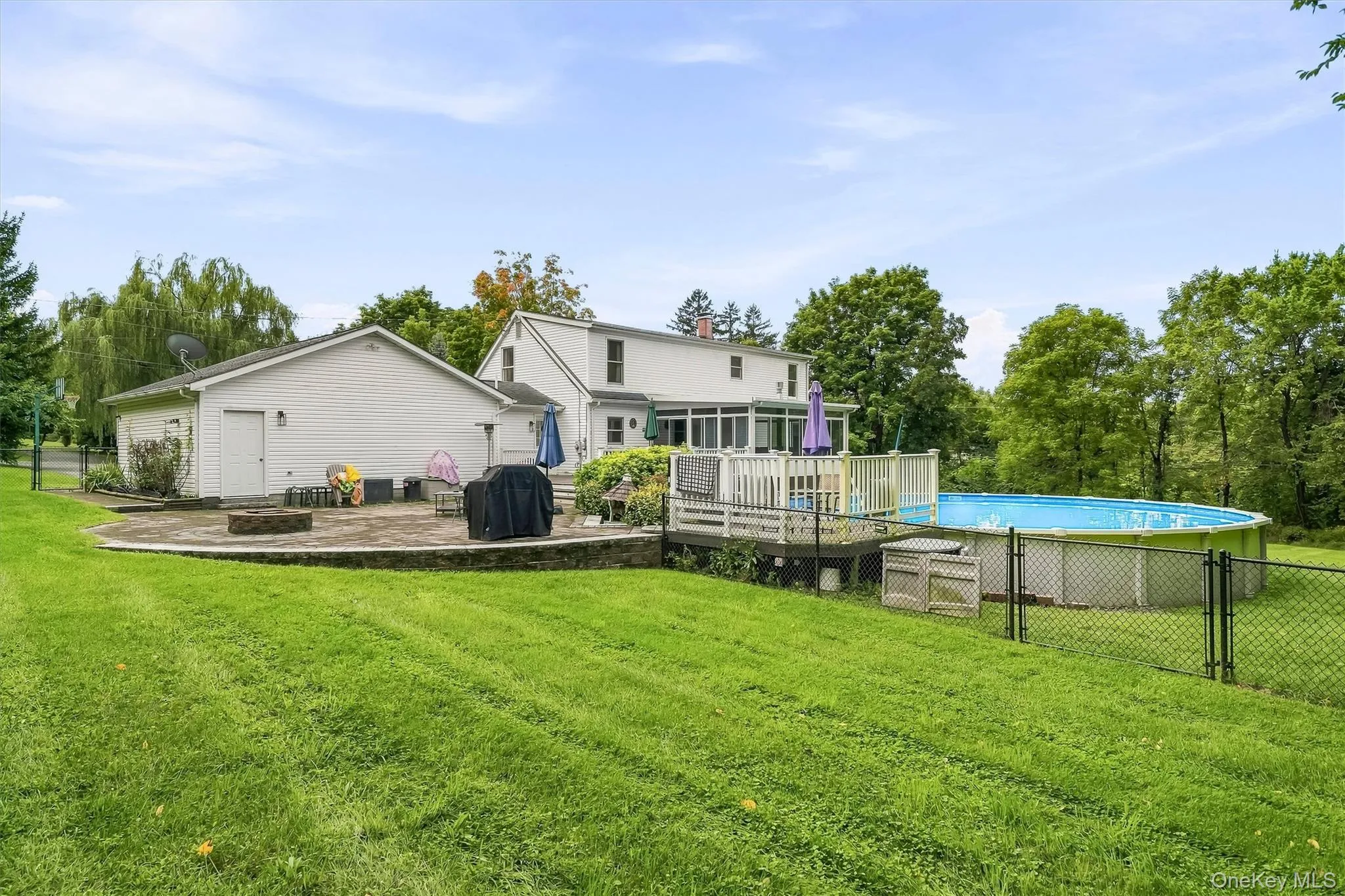 Expansive green lawn, stone patio, attached garage, rear deck, and fenced above-ground pool Expansive green lawn, stone patio, attached garage, rear deck, and fenced above-ground pool
